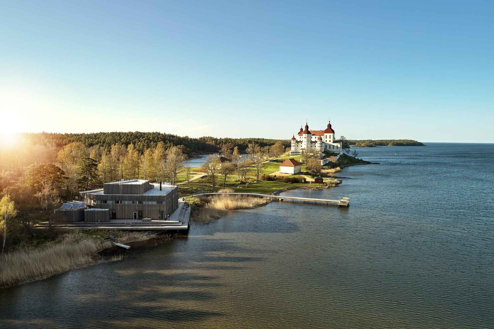 Schloss Läckö, ein weißes Schloss und Naturum, ein Gebäude aus Holz stehen am Seeufer in Westschweden.