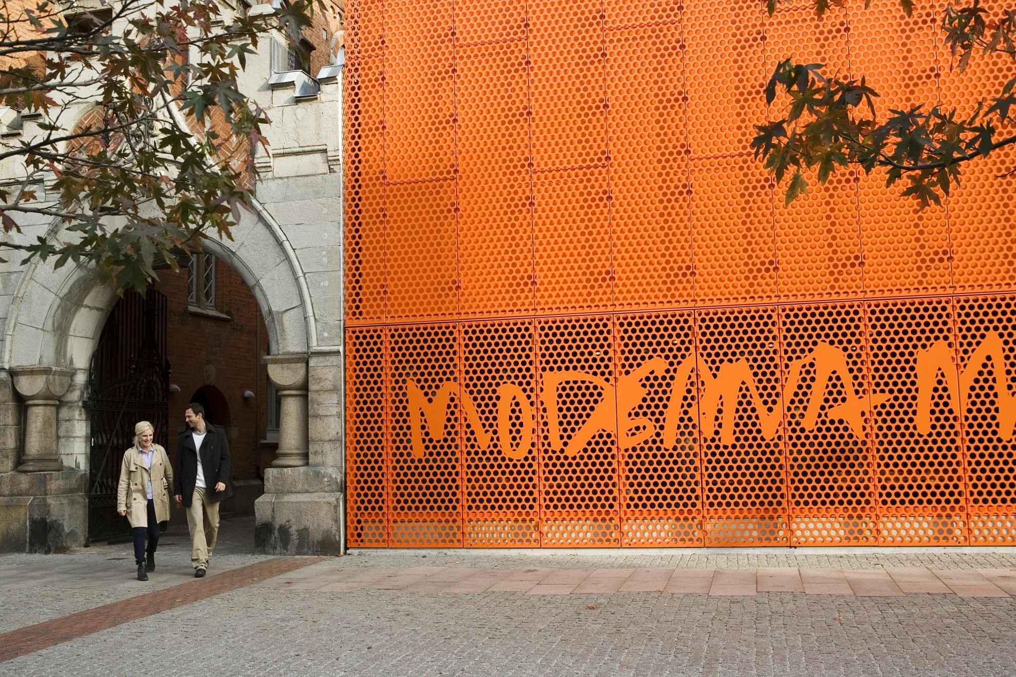 Ein Mann und eine Frau gehen draußen am orangefarbenen Schild des Moderna Museet in Malmö vorbei.