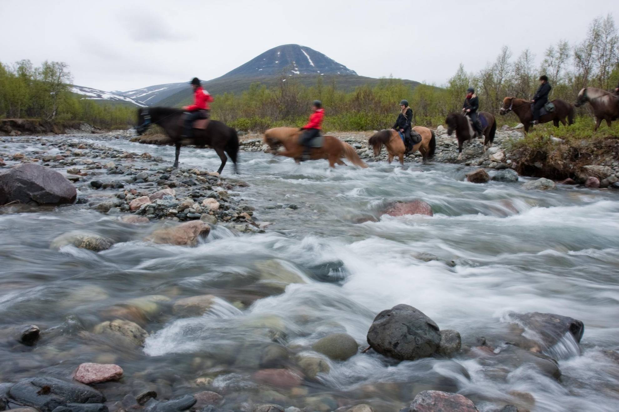 Menschen auf Pferden überqueren einen Bach in Schwedisch-Lappland.