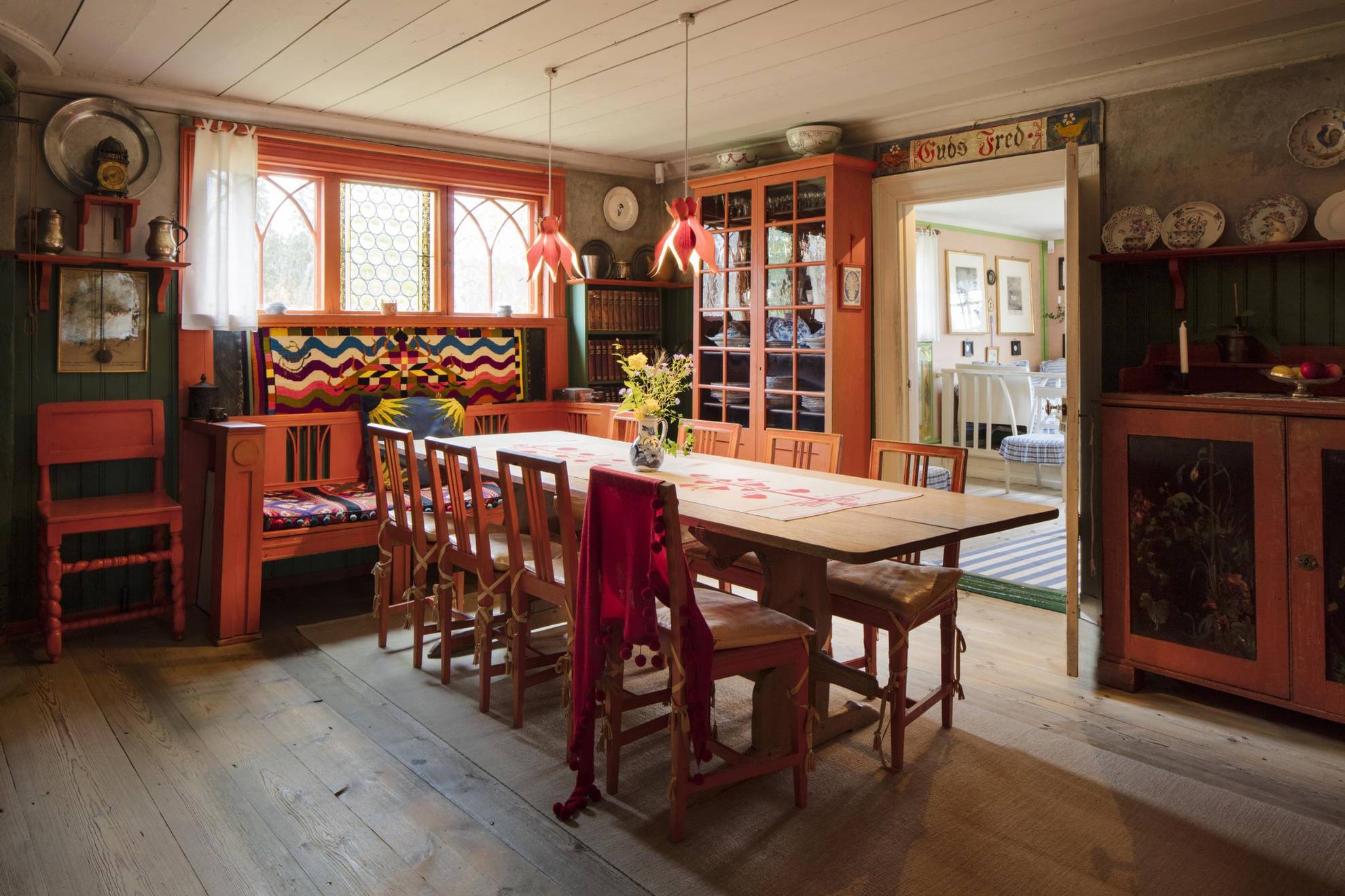 Historical Swedish interior design at Lilla Hyttnäs, with a large dinner table, red wooden furniture and historical porcelain on some walls.