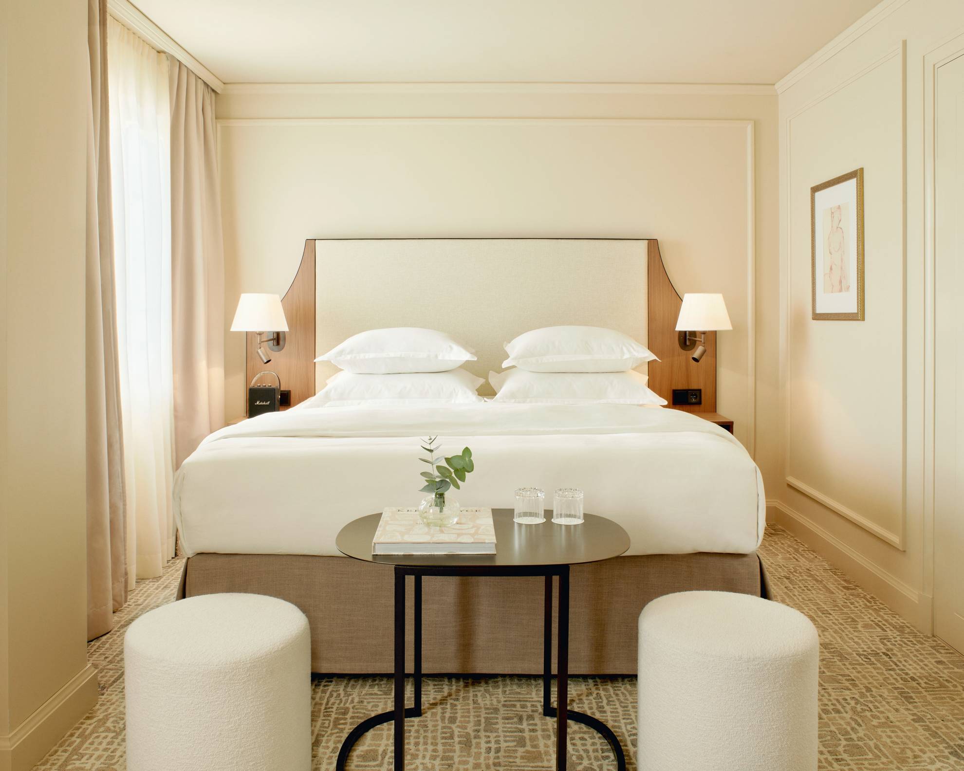 Ein Hotelzimmer in der Villa Dahlia. Das Zimmer hat helle Wände, ein Doppelbett, einen dunklen kleinen Tisch und zwei weiße Sitzpolster.