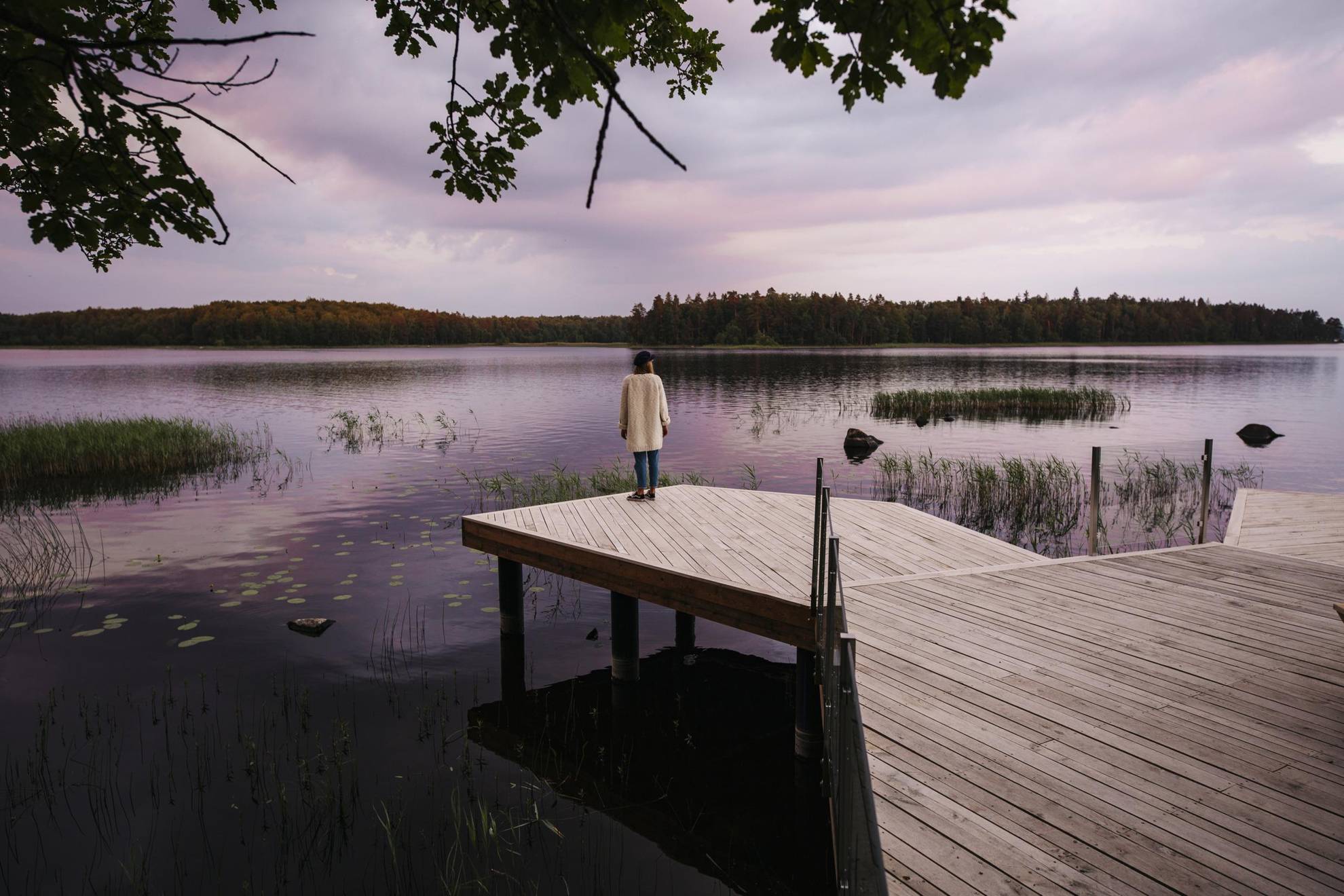 Eine Frau steht am Rand eines Stegs und genießt den Blick auf einen See.
