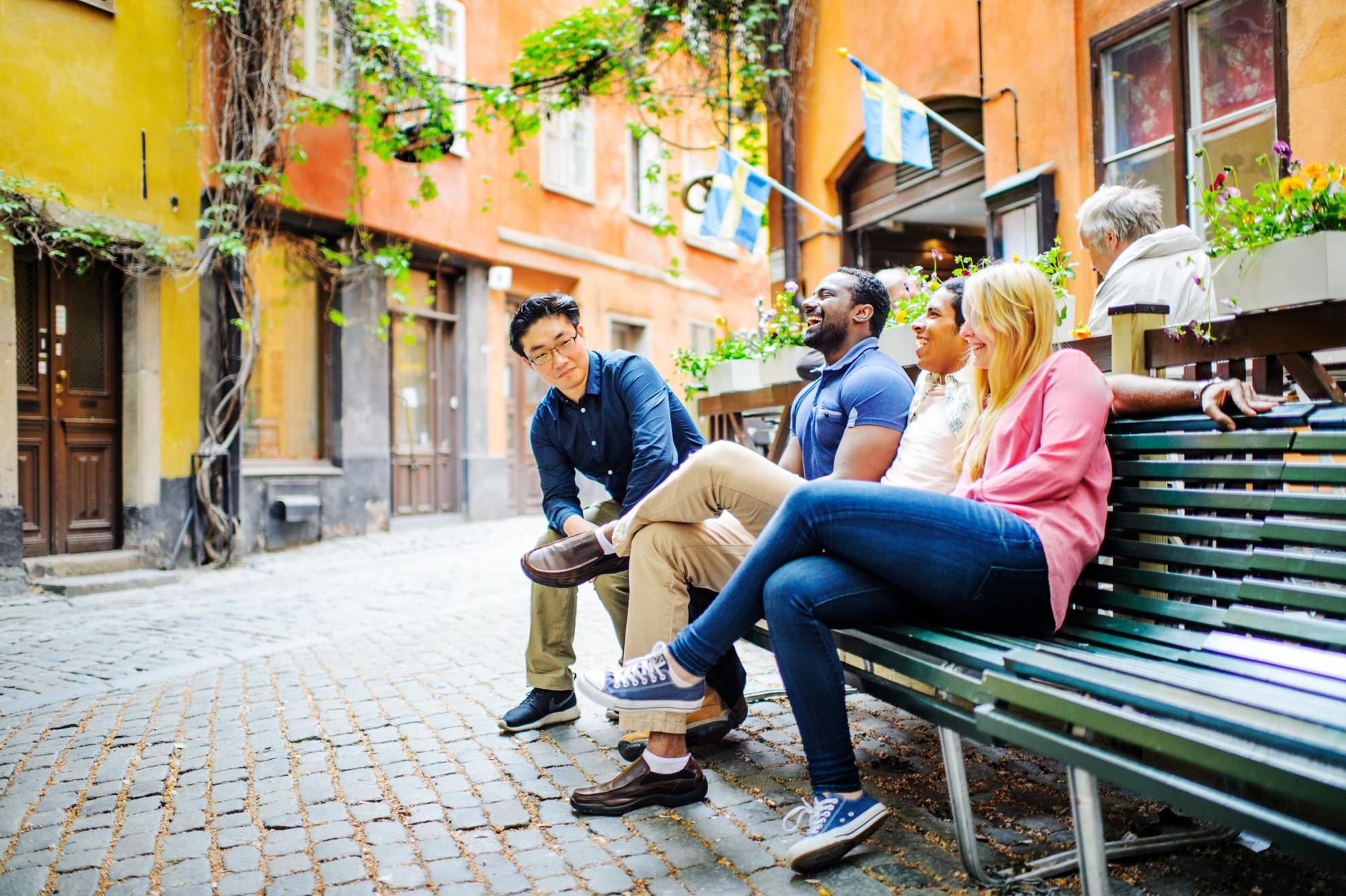 A group of people are sitting on a bench in Old Town Stockholm, talking and laughing.