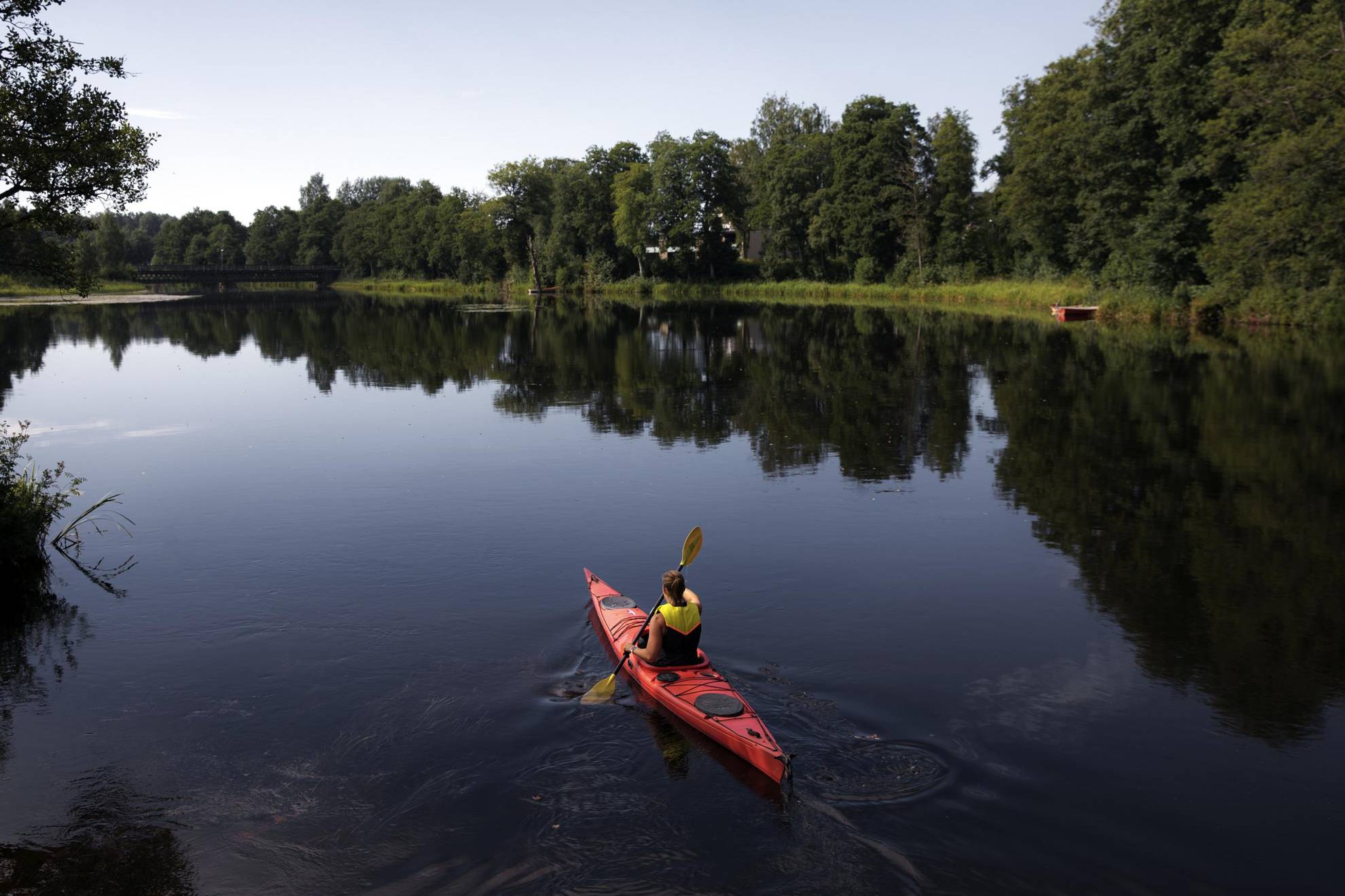 Eine Person fährt im Sommer Kajak auf einem ruhigen See.