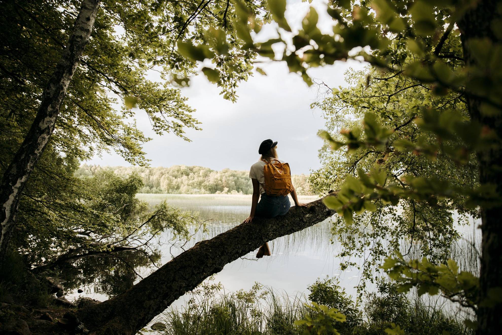 Eine Person mit Rucksack sitzt auf einem Dreier und blickt auf einen See.