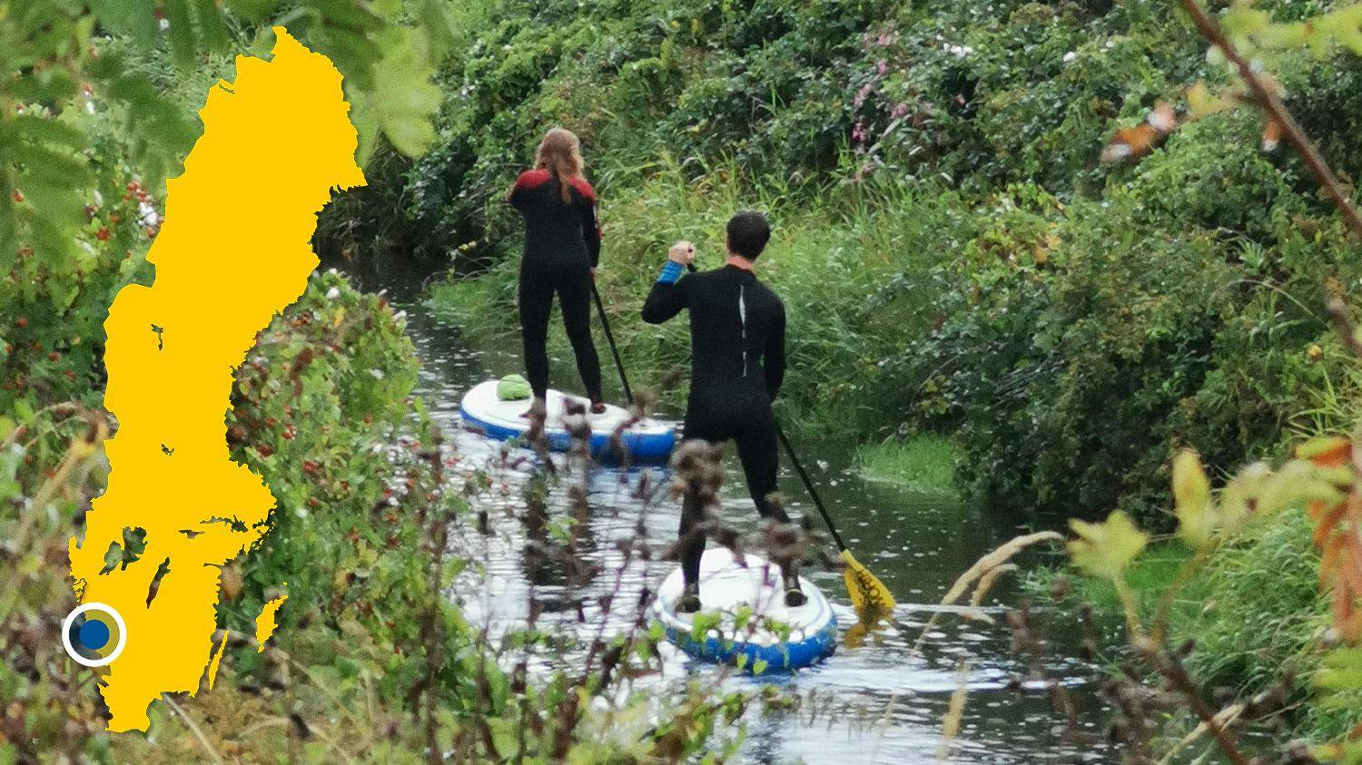 Zwei Personen paddeln auf Stand Up Paddleboards in einem schmalen Fluss. Es gibt eine gelbe Karte von Schweden mit einer Markierung, die Himleån lokalisiert.