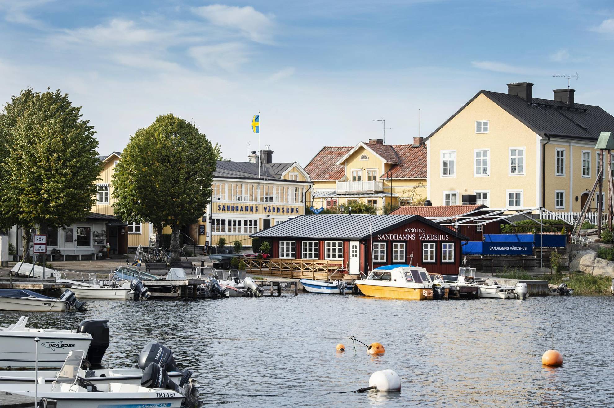 Häuser in Gelb und Rot, gelegen an einem Hafen mit vielen kleinen Booten in Sandhamn.