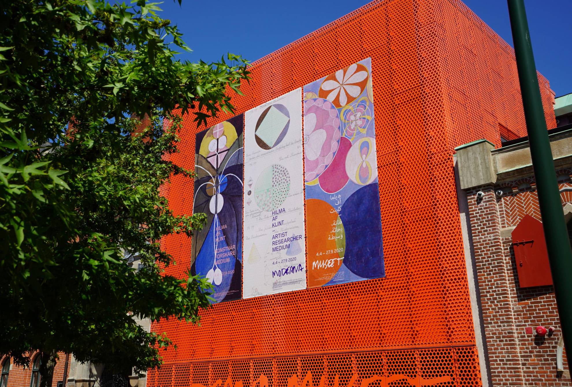 Ein Gebäude mit einer orangenen Fasade und einigen bunten Plakaten daran, so sieht das Moderna Museet in Malmö aus.