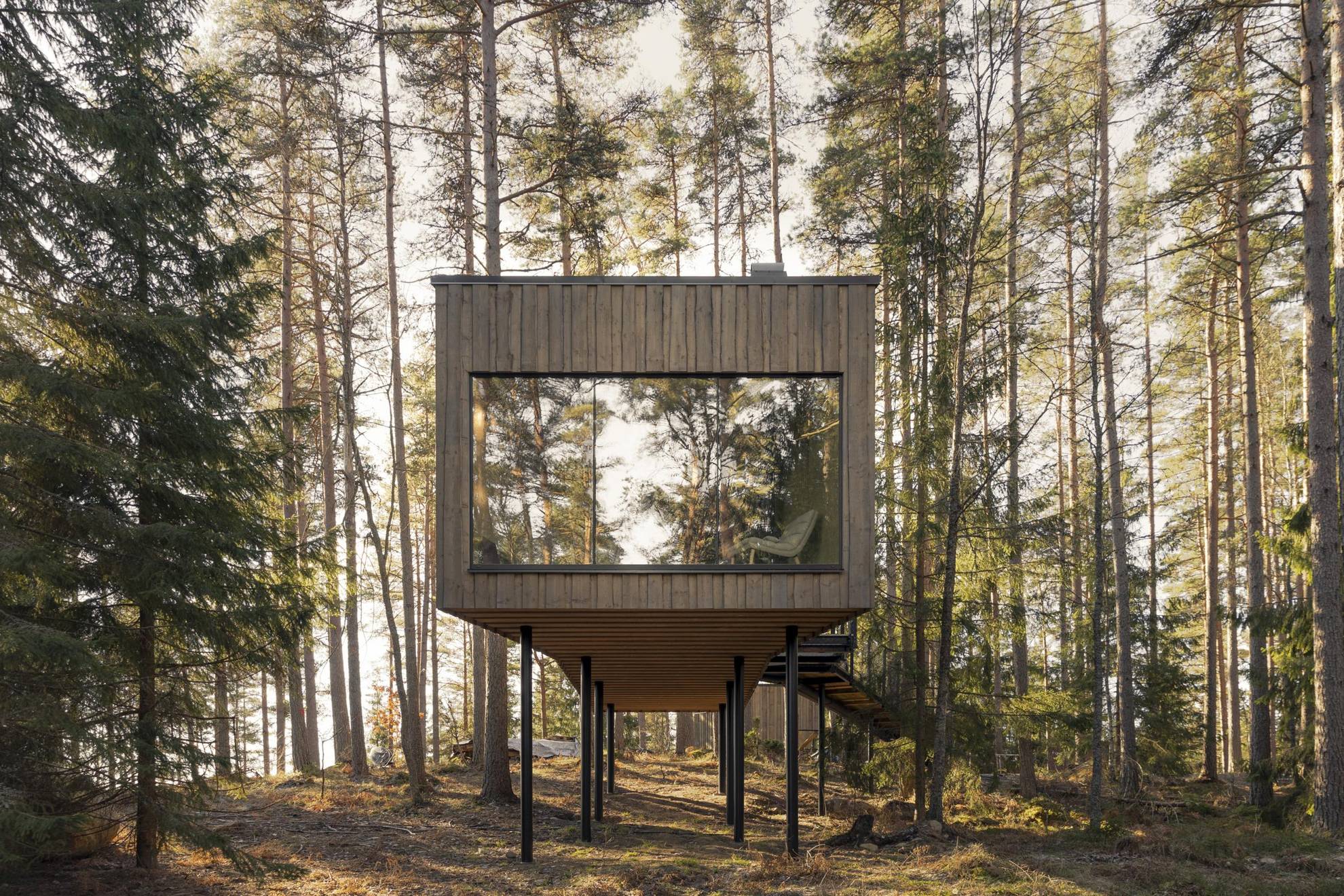 Eine rechteckige Holzsuite mit einem riesigen Fenster befindet sich in einem Wald.
