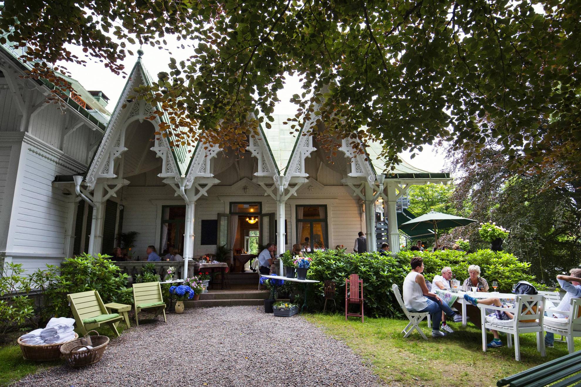 Außenansicht des Restaurants der Villa Sjötorp in Westschweden an einem sonnigen Tag. Die Restaurantgäste sitzen auf Gartenmöbeln an Tischen.