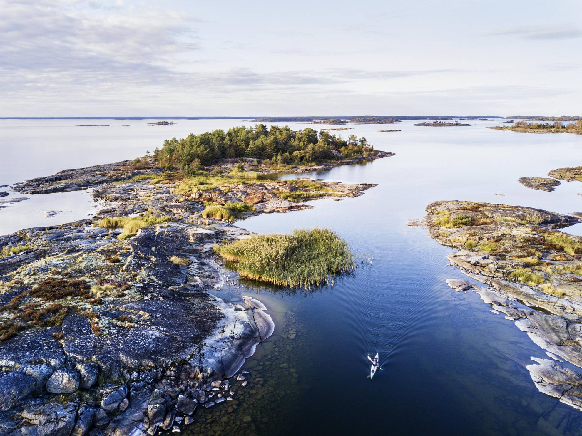 Eine Person fährt im Sommer mit dem Kajak zwischen kleinen Inseln im Vänernsee.