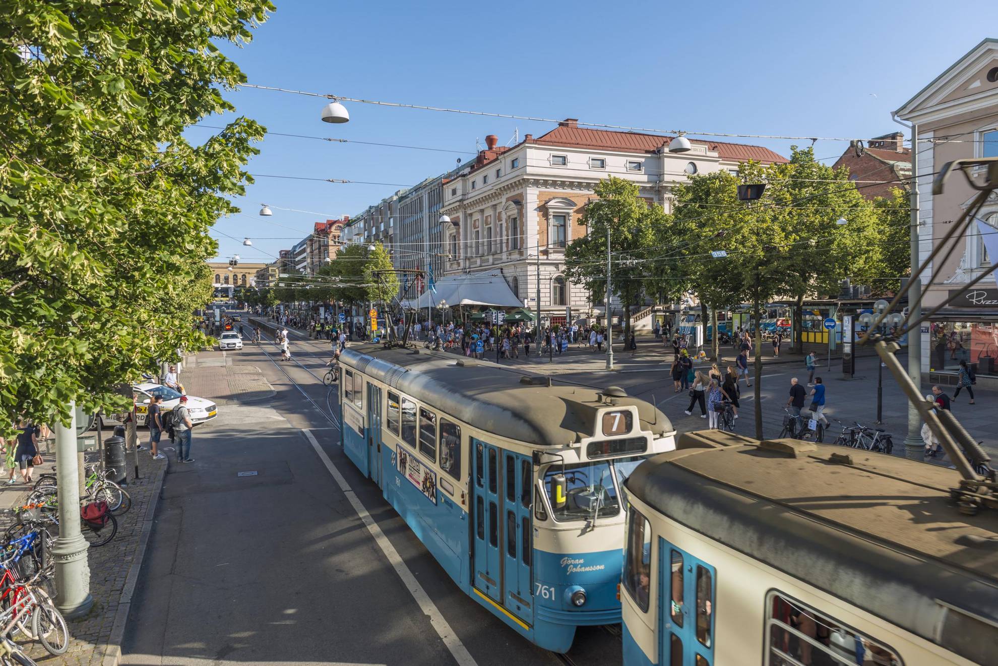 A classic tram passes the street Avenyn in Gothenburg, busy with pedestrians and lined with trees.