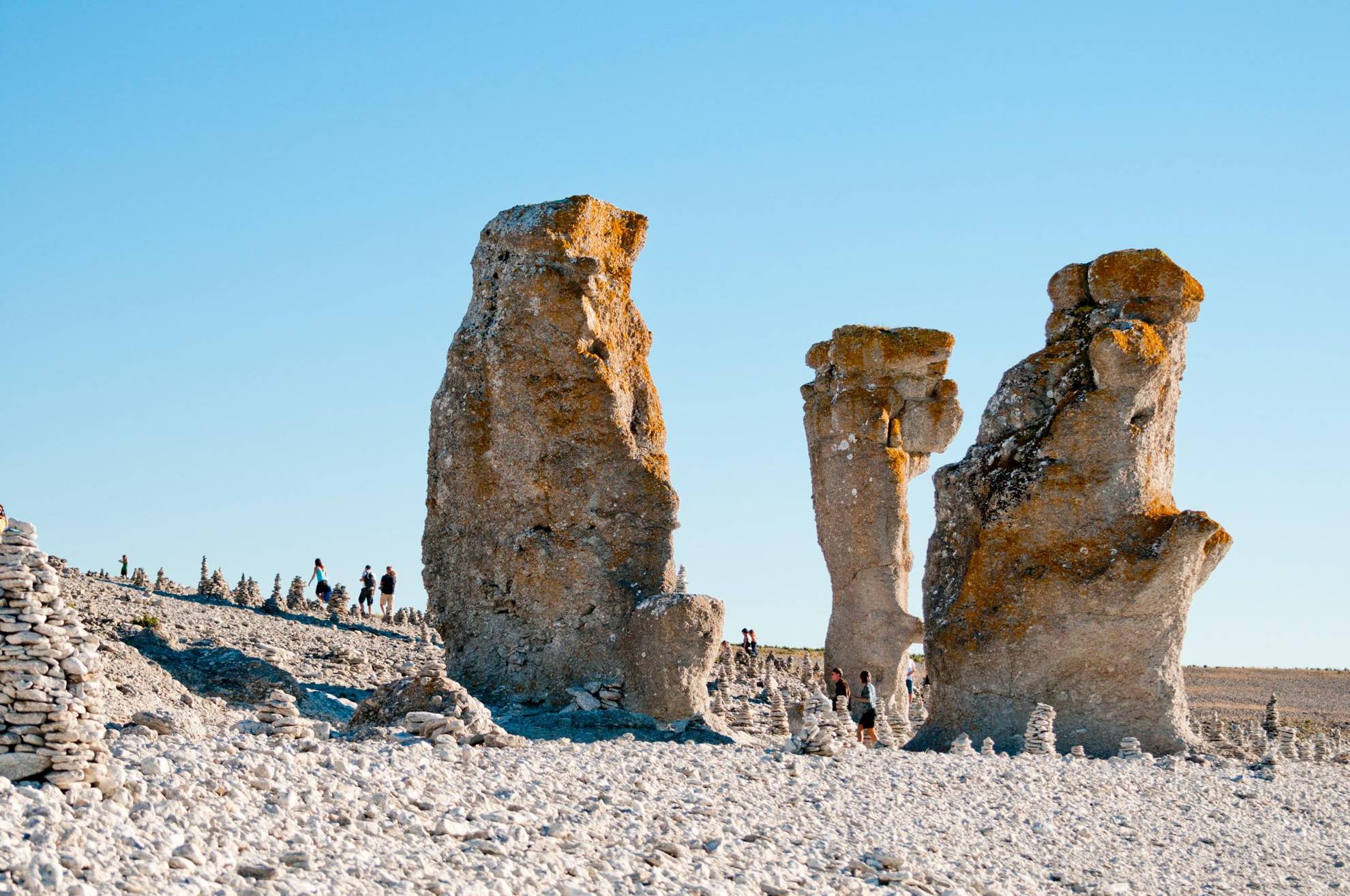 Drei hohe Kaltsteingebilde stehen auf einem steinigen Strand.