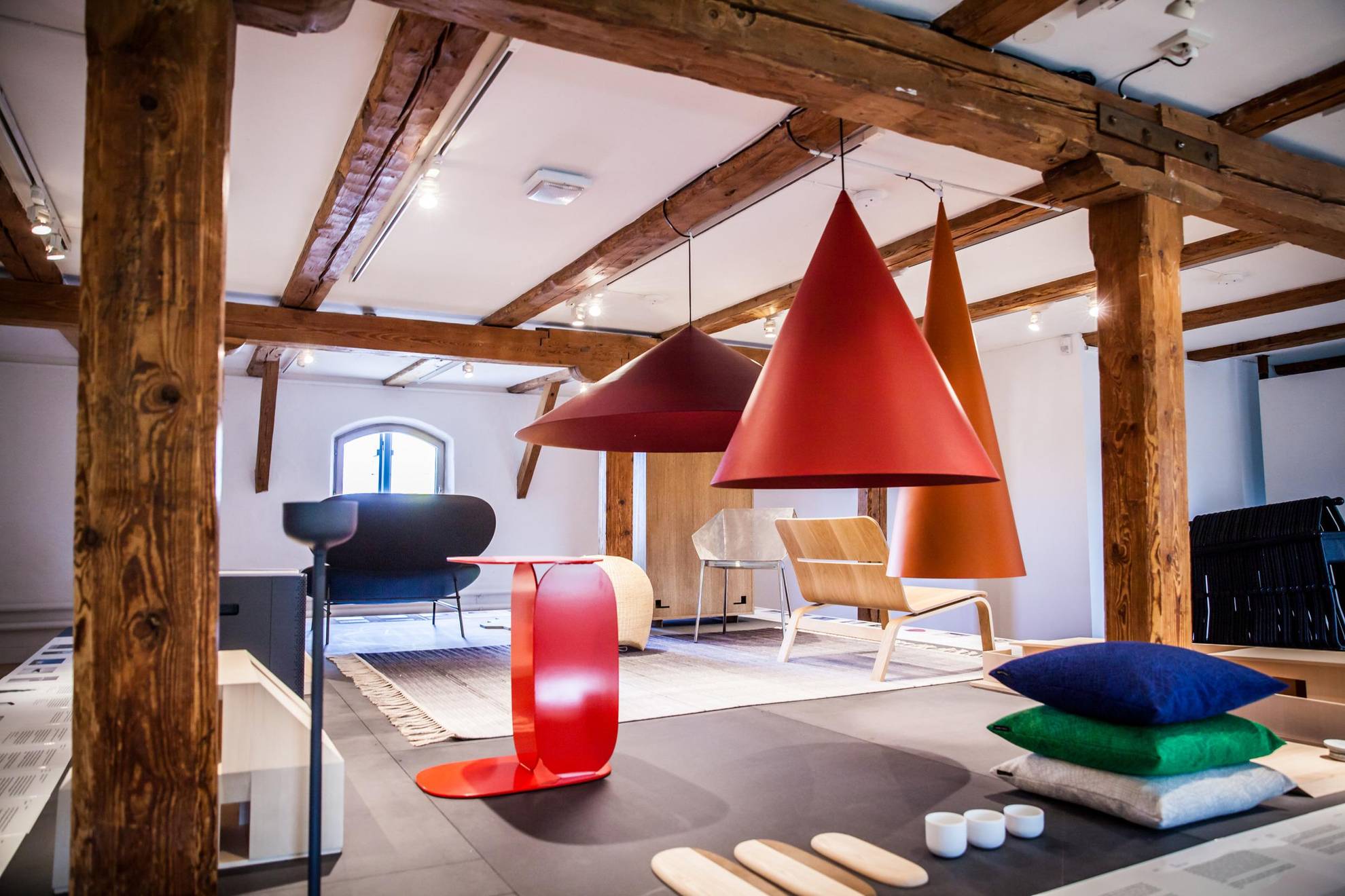 Ein Dachzimmer mit Holzbalken. Bunte Designobjekte im Raum, wie Lampen, Stühle und Kissen.