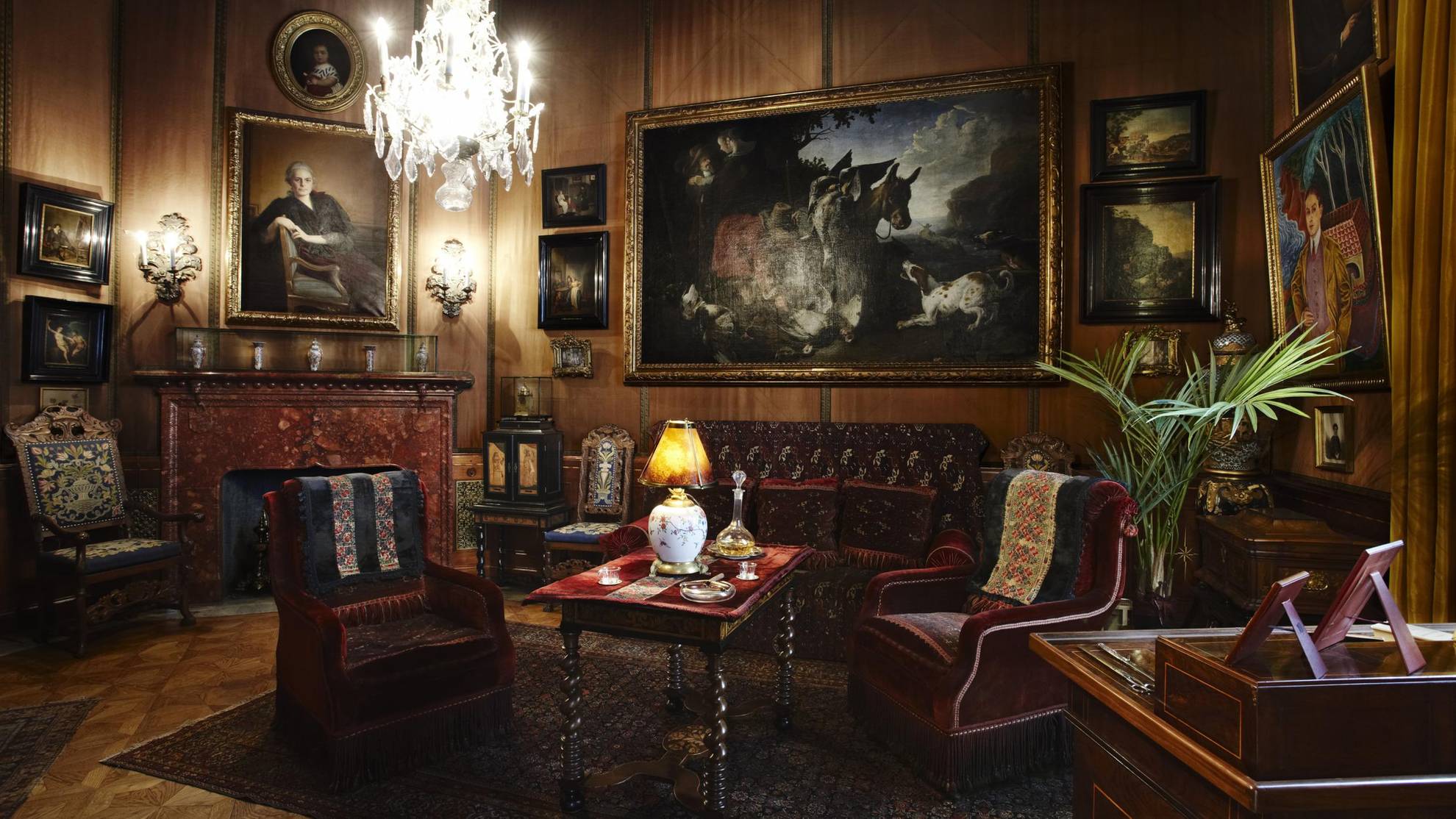 Der Luxus im Palast Hallwyl mit dunkelroten Samtmöbeln, großen Gemälden und einem Kronleuchter.