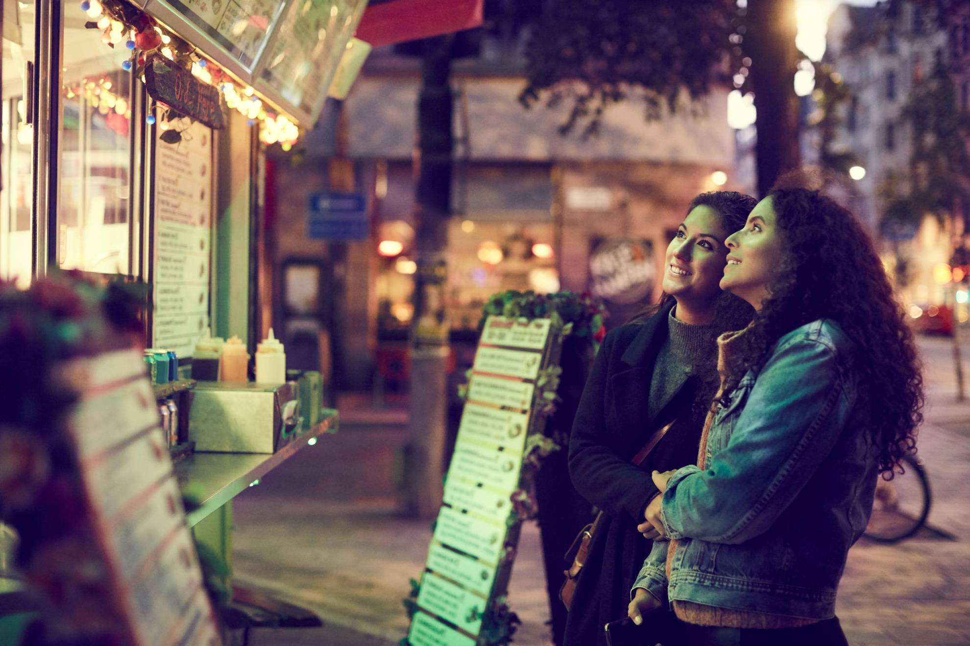 Zwei Frauen schauen sich vor einem Kiosk eine Speisekarte an.
