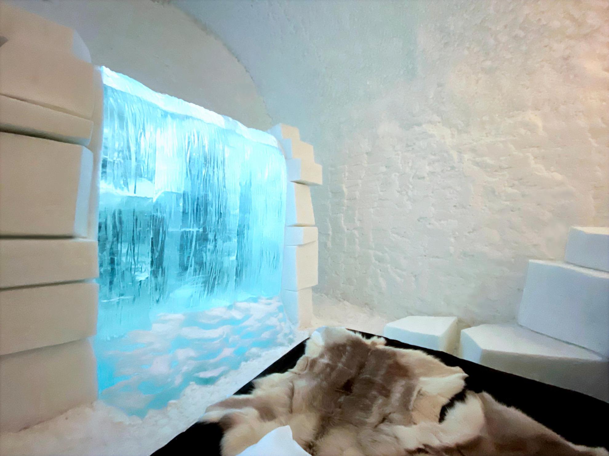 Ein Wasserfall aus Eis schmückt einen Raum aus Schnee und Eis. Vorne liegen Rentierfelle.