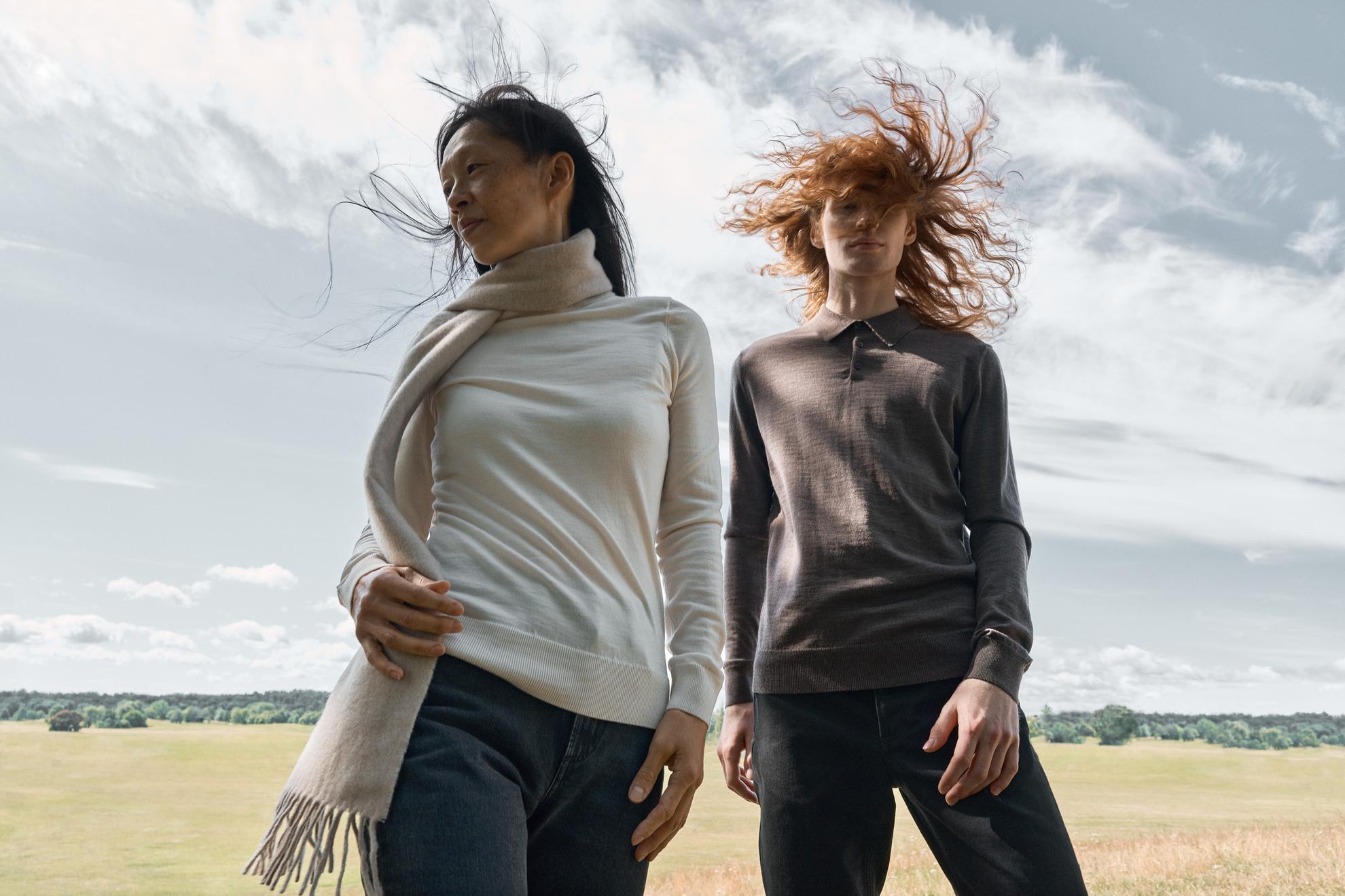 Ein Modeshooting mit zwei Frauen, die auf einem Feld stehen und den Wind in ihren Haaren spüren.