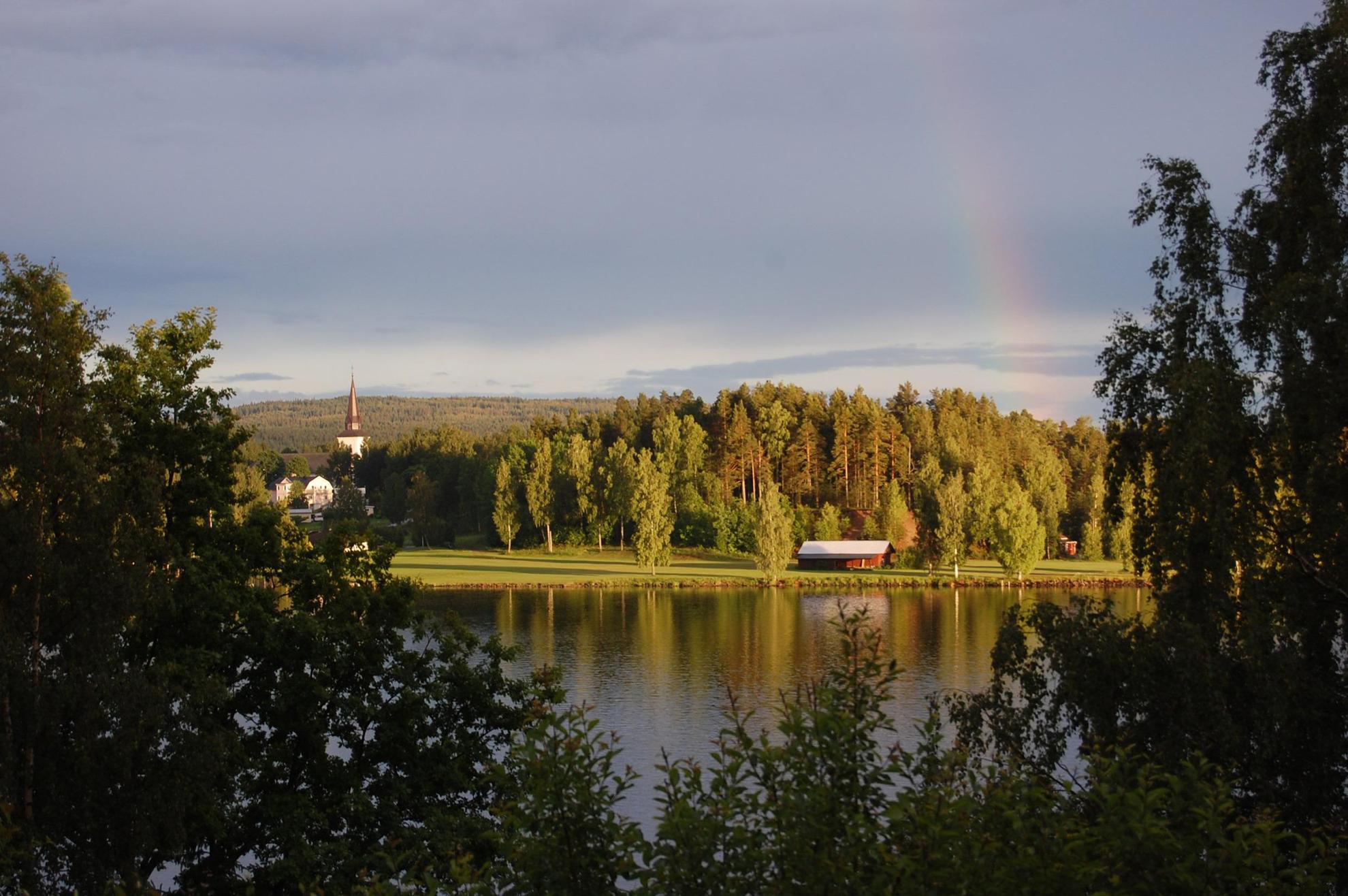 Looking across Lake Fryken is a rainbow, forest, a church steeple and a barn.
