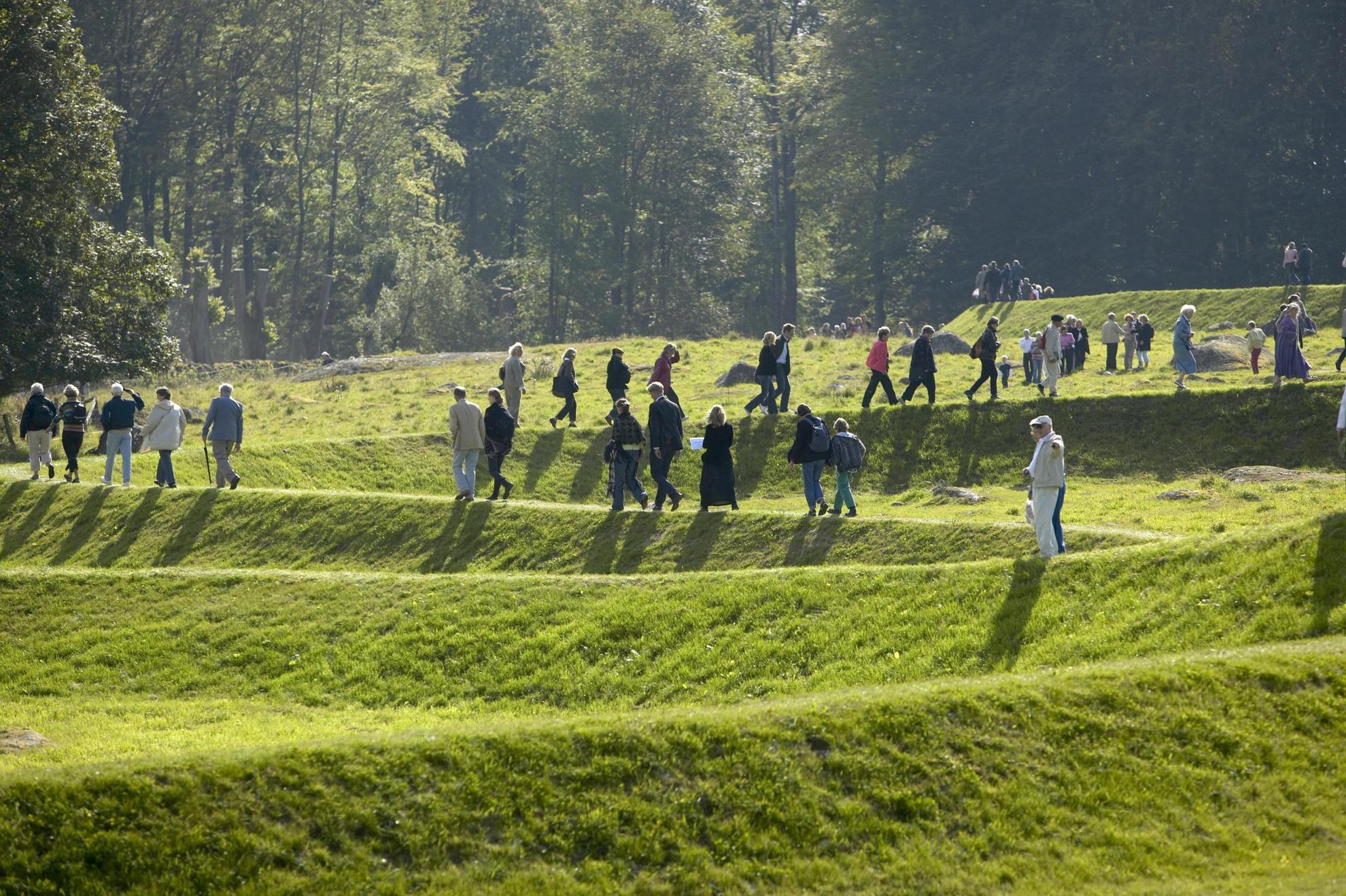 Ein Kunstwerk namens „Eleven Minute Line“ in einem Skulpturenpark. Mehrere Menschen laufen auf dem Kunstwerk, einem 500 Meter langen, gewundenen Grat aus Erde, Stein und Gras.
