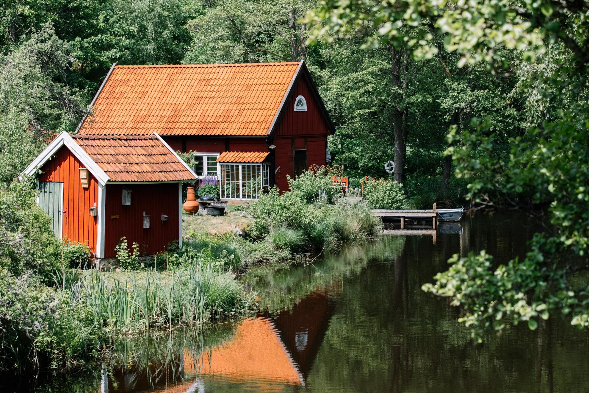 Neben einem See mit üppigem Wald drumherum gibt es ein traditionelles rotes Häuschen und ein kleines rotes Gästehaus.