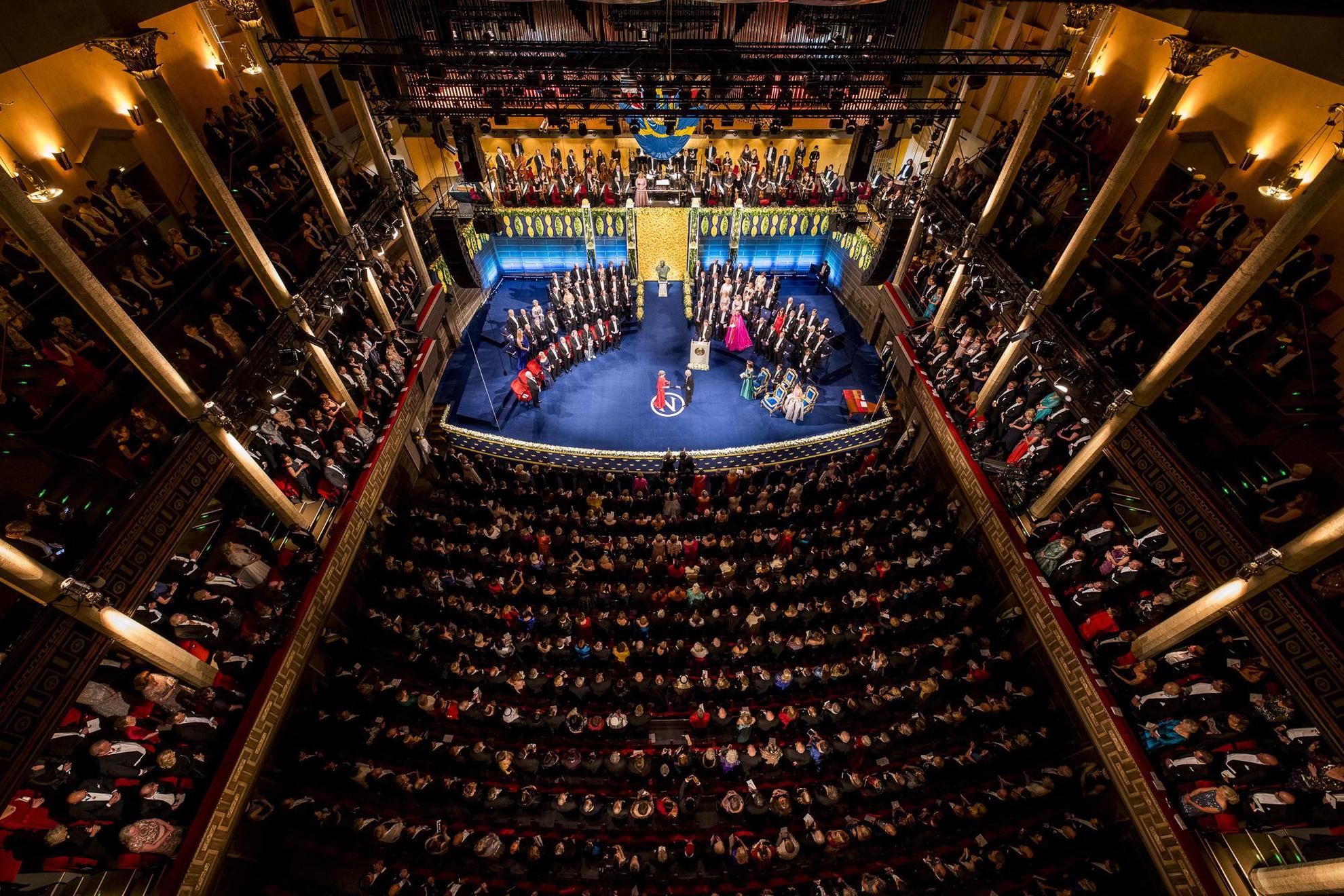 Ein Saal voller Menschen, die auf die Bühne schauen, auf der die Preisträger ihren Nobelpreis erhalten.