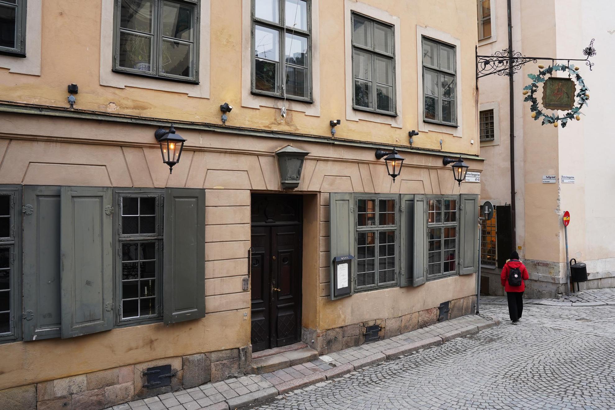 Außenansicht von Den Gyldene Freden in der Altstadt von Stockholm. Die Fassade des Gebäudes ist beige und das Restaurant hat grüne Fenster und eine braune Doppeltür.
