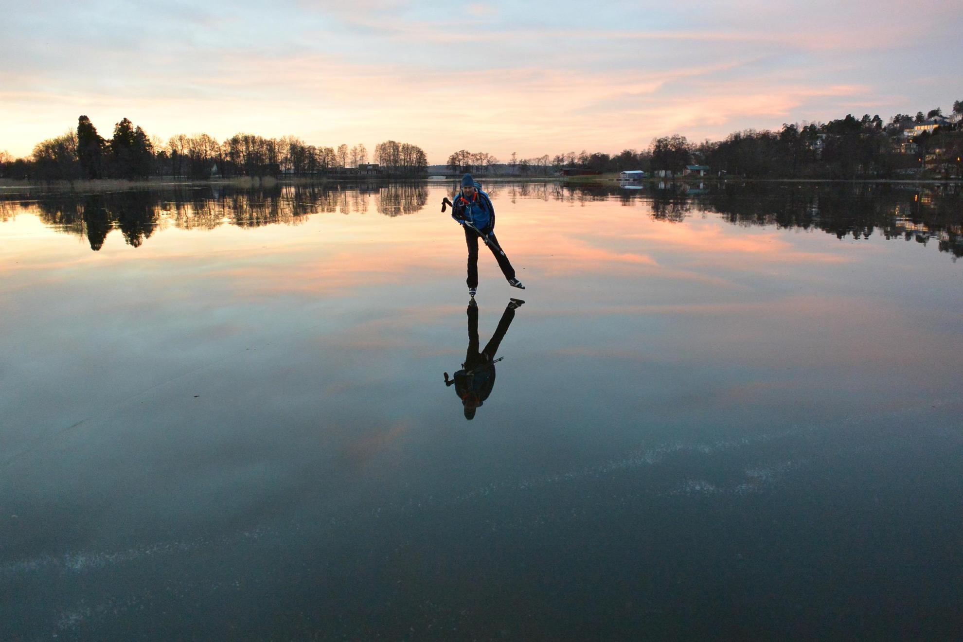 Eine Person läuft Schlittschuh auf einem zugefrorenen See in der Abenddämmerung.