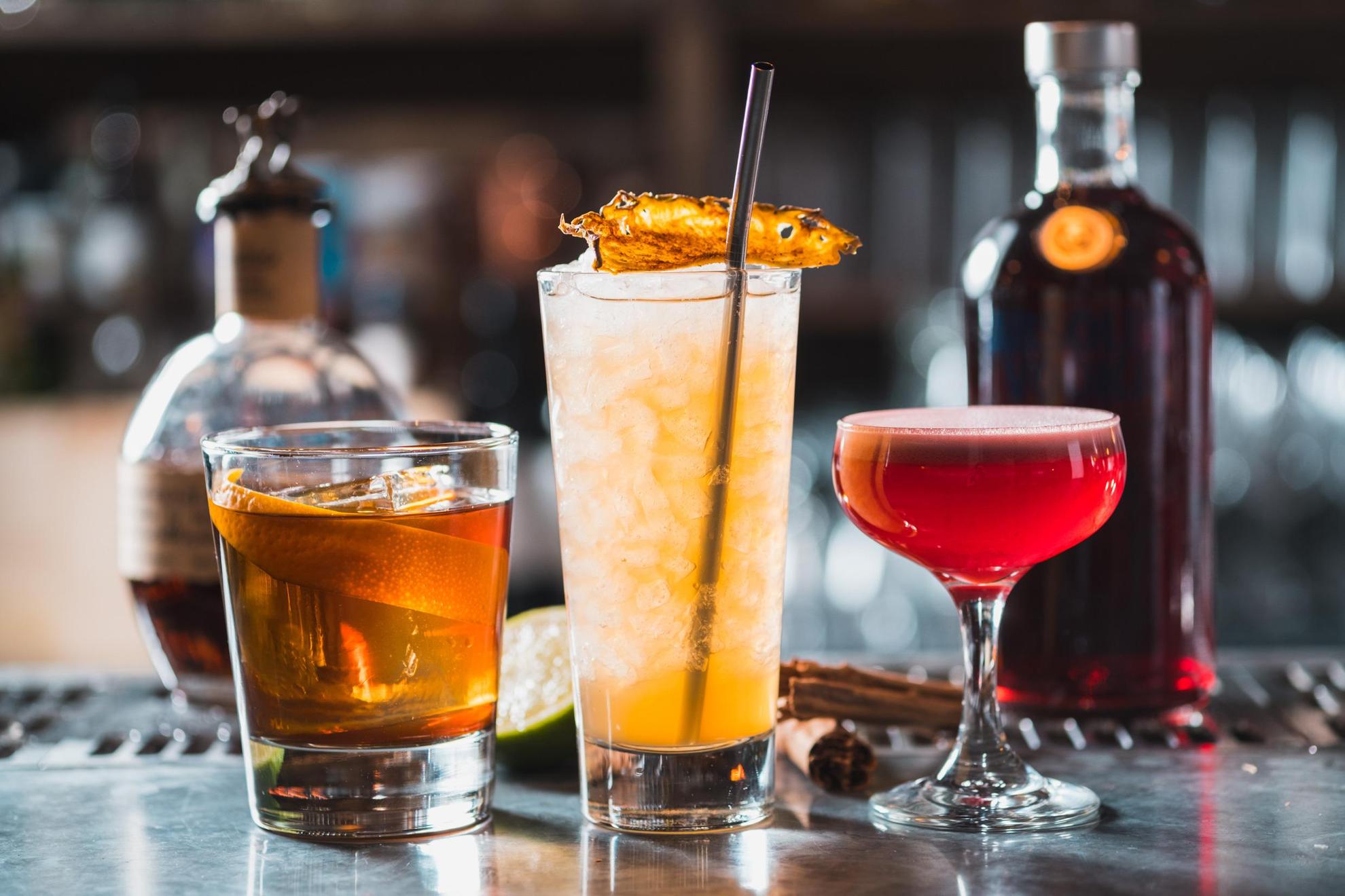 Drei verschiedene Cocktails stehen auf einem Tresen an einer Bar.