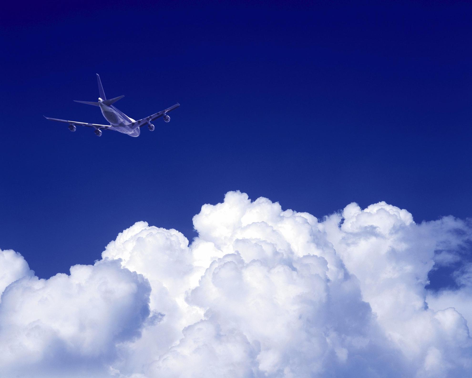 An airplane flies above white clouds.
