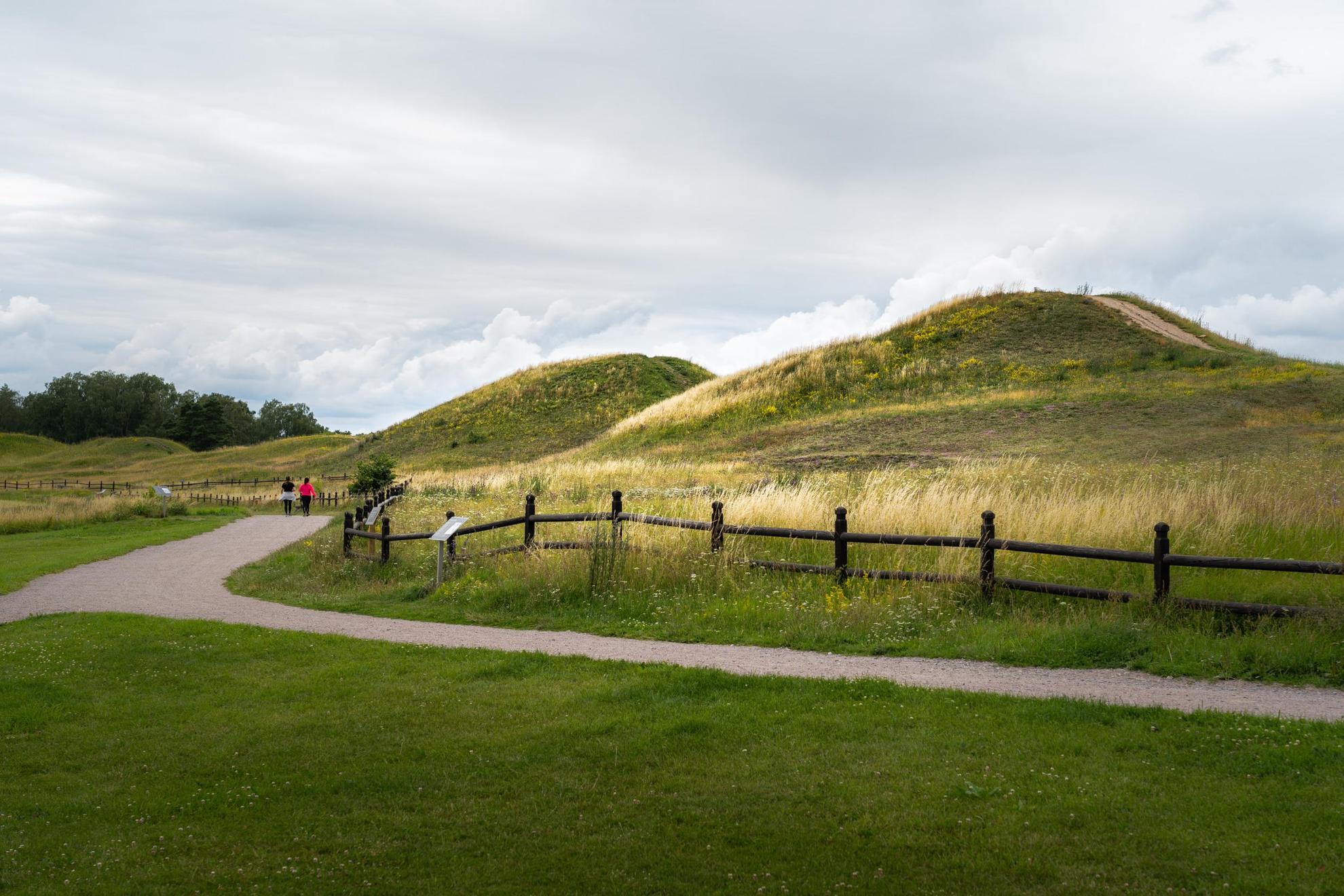 Ein Kiesweg befindet sich neben großen Hügeln, die mit Gras bedeckt sind.