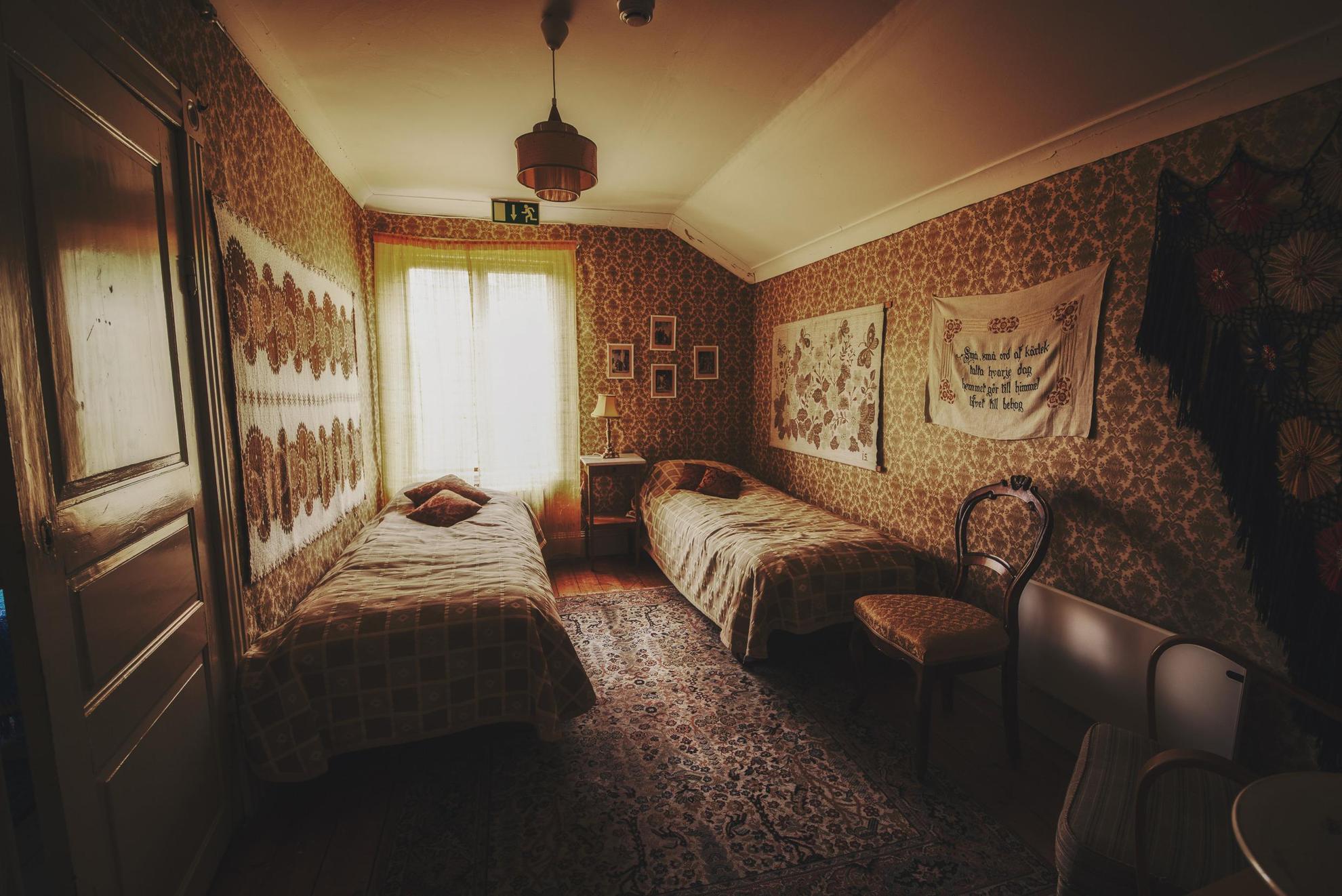 Ein Zimmer mit dekorativer Tapete, Gemälden, einem Teppich, einem Stuhl und zwei Einzelbetten.