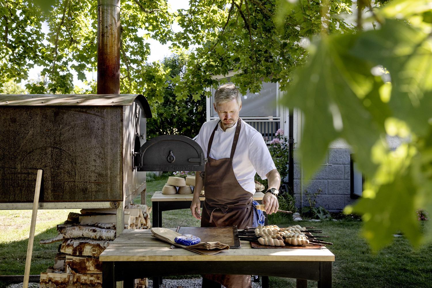 Ein Koch steht an einem Holzofen in einem Garten.
