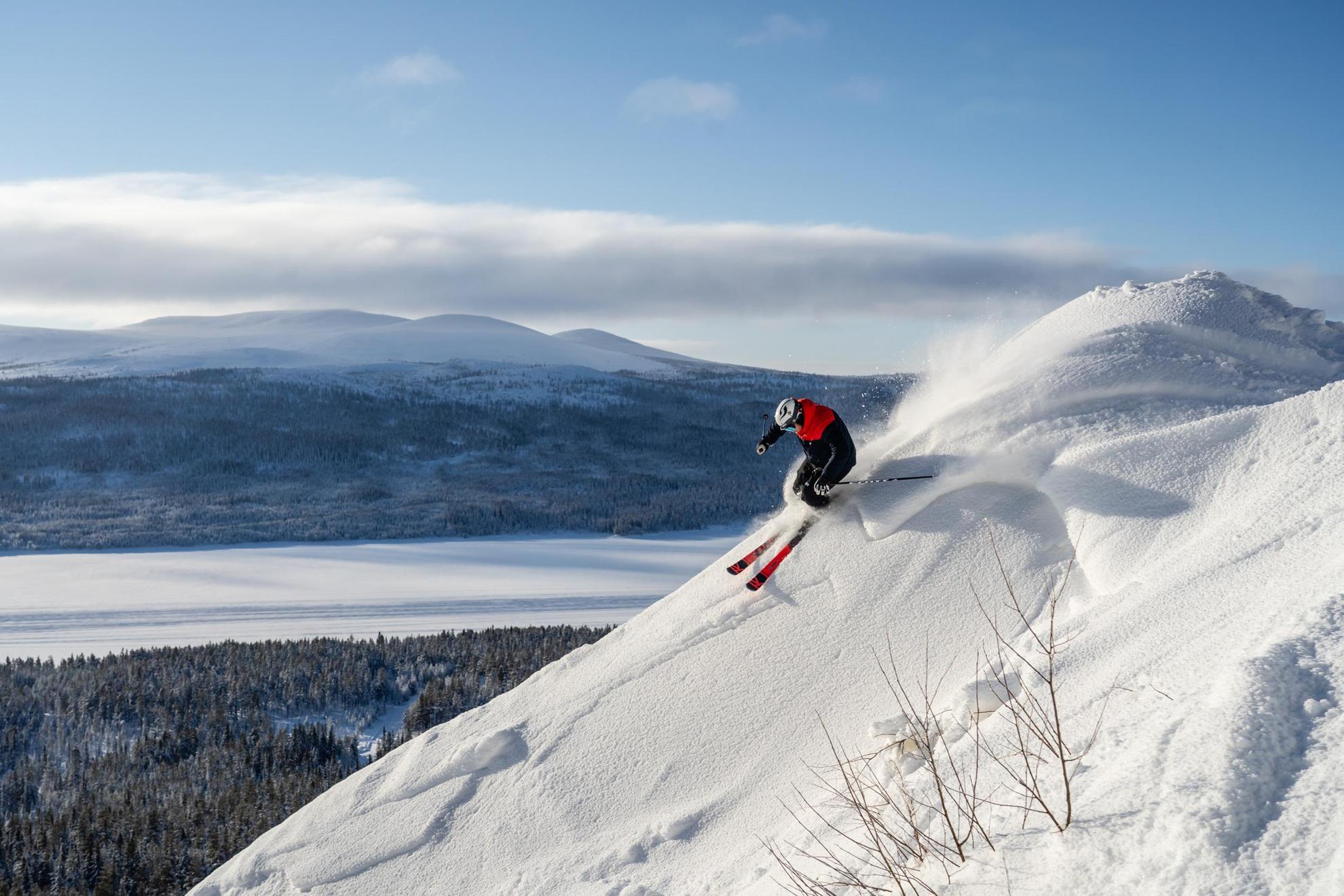 Eine Person beim Skifahren auf einem Berg mit Blick auf eine verschneite Landschaft im Hintergrund.