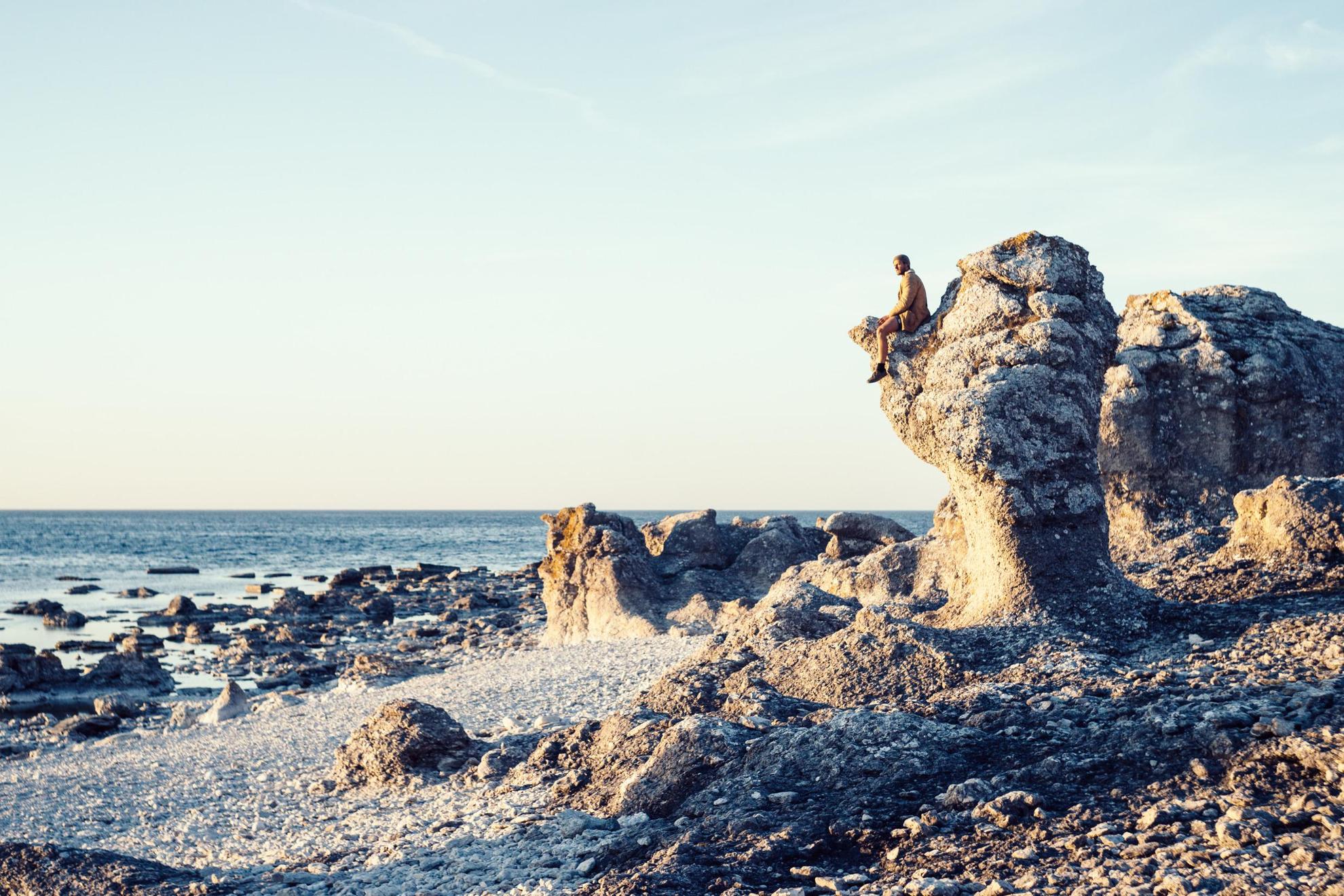 Eine Person sitzt auf einem hohen Kalksteingebilde, wovon mehrere an einem Meeresstrand stehen.