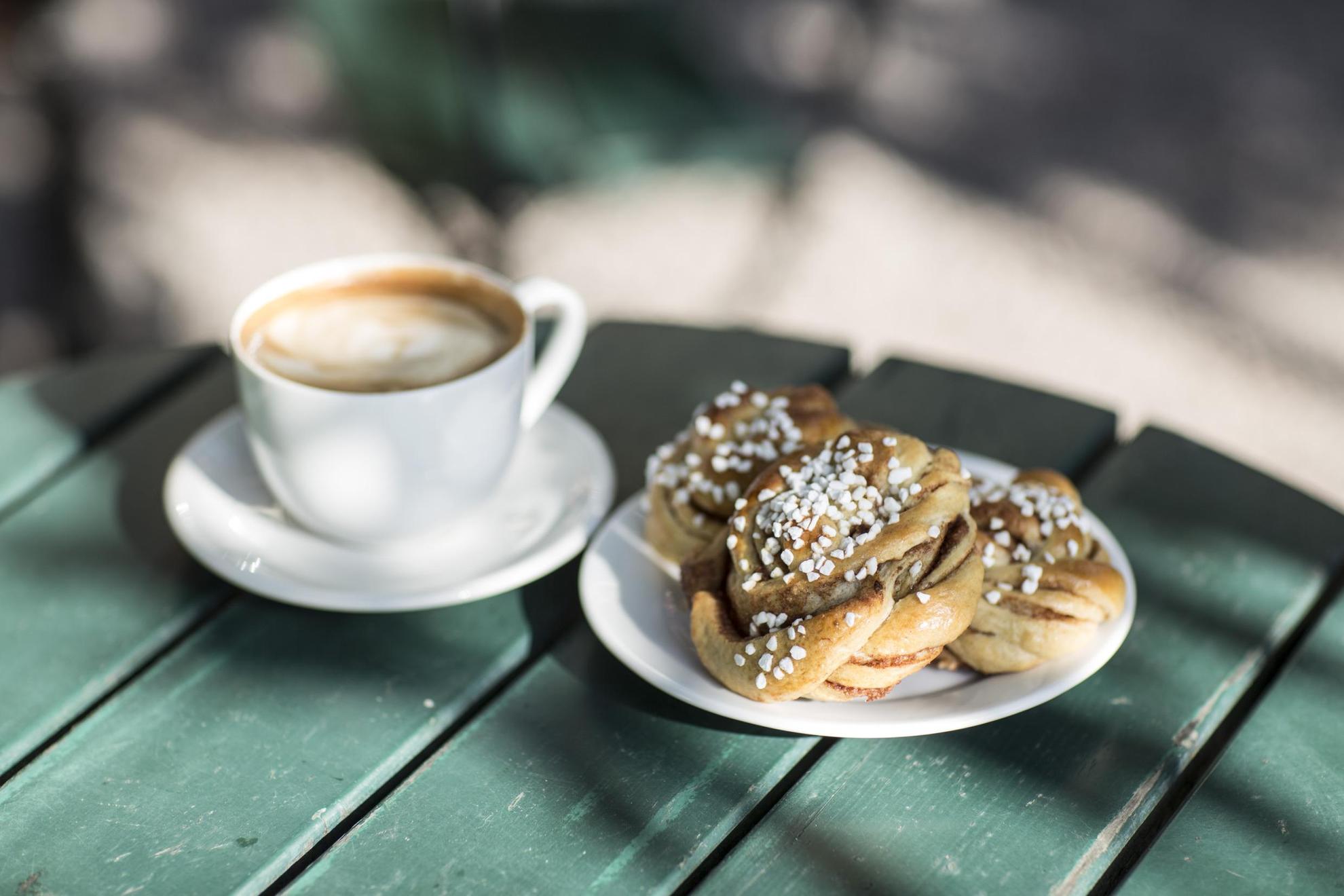 Eine Tasse Kaffee und eine Zimtschnecke stehen auf dem Tisch eines gemütlichen Cafés in Schweden.