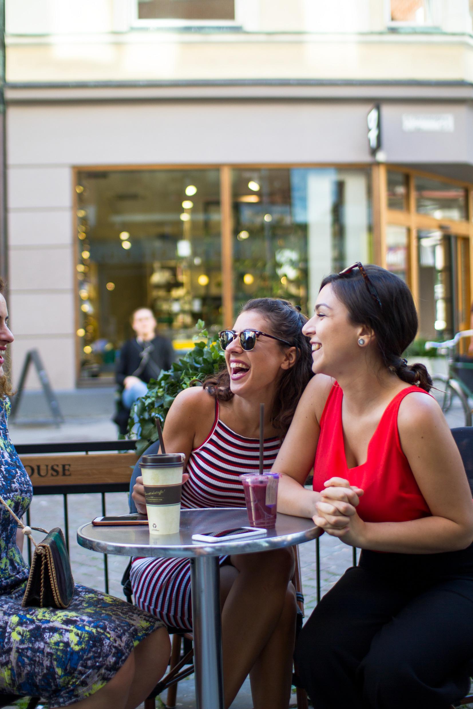 Drei Frauen, die im Freien in Malmö Kaffee und andere Getränke trinken und dabei lächeln und lachen.