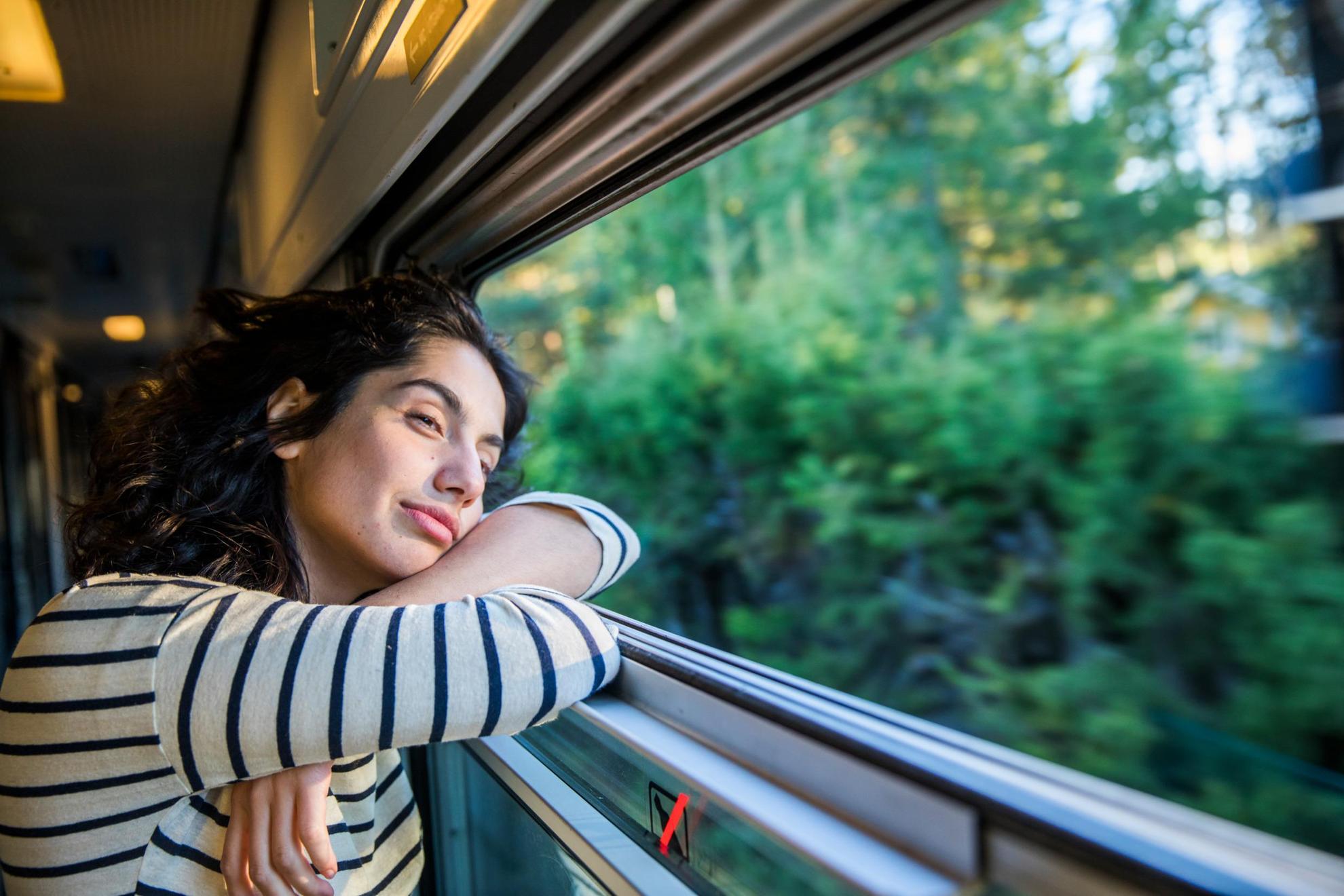 Eine Frau schaut in einem Zug in Schweden aus dem Fenster, während sie durch Wald und Grün fährt.