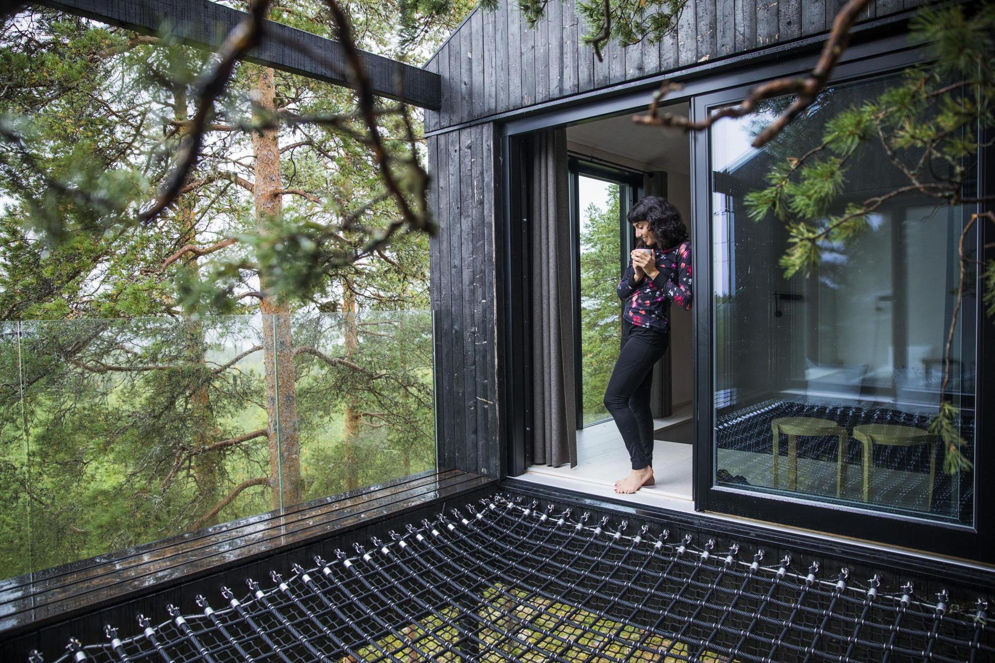 Eine Person genießt den Ausblick auf die schwedischen Wälder aus einem modernen Baumhaushotel heraus.
