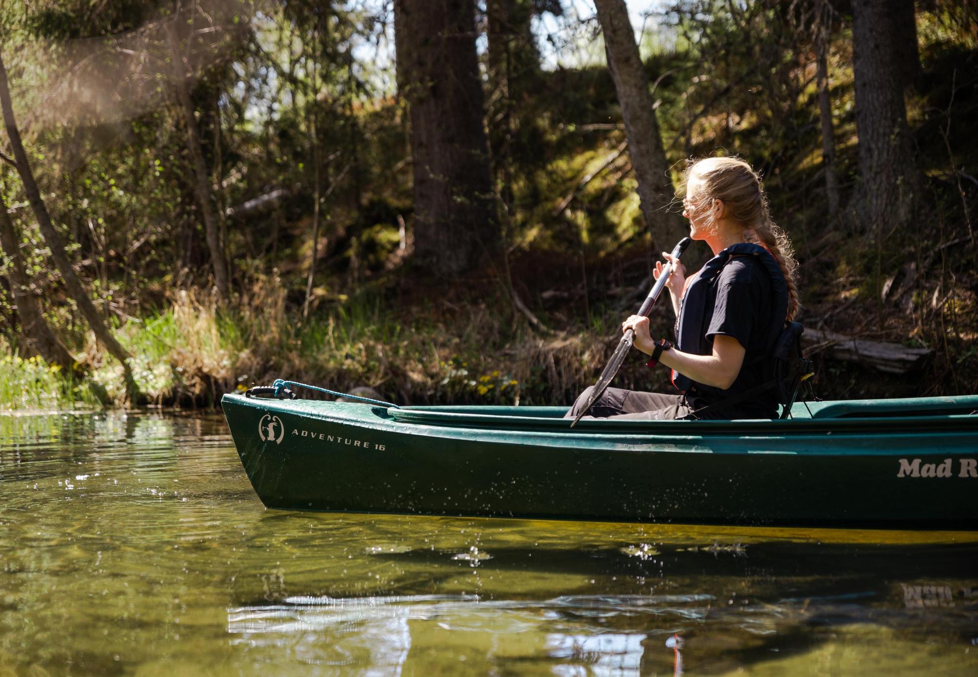 Eine Frau fährt mit dem Kanu auf dem Tavelsjön See Umeå. Im Hintergrund sieht man Wald und Grünflächen.