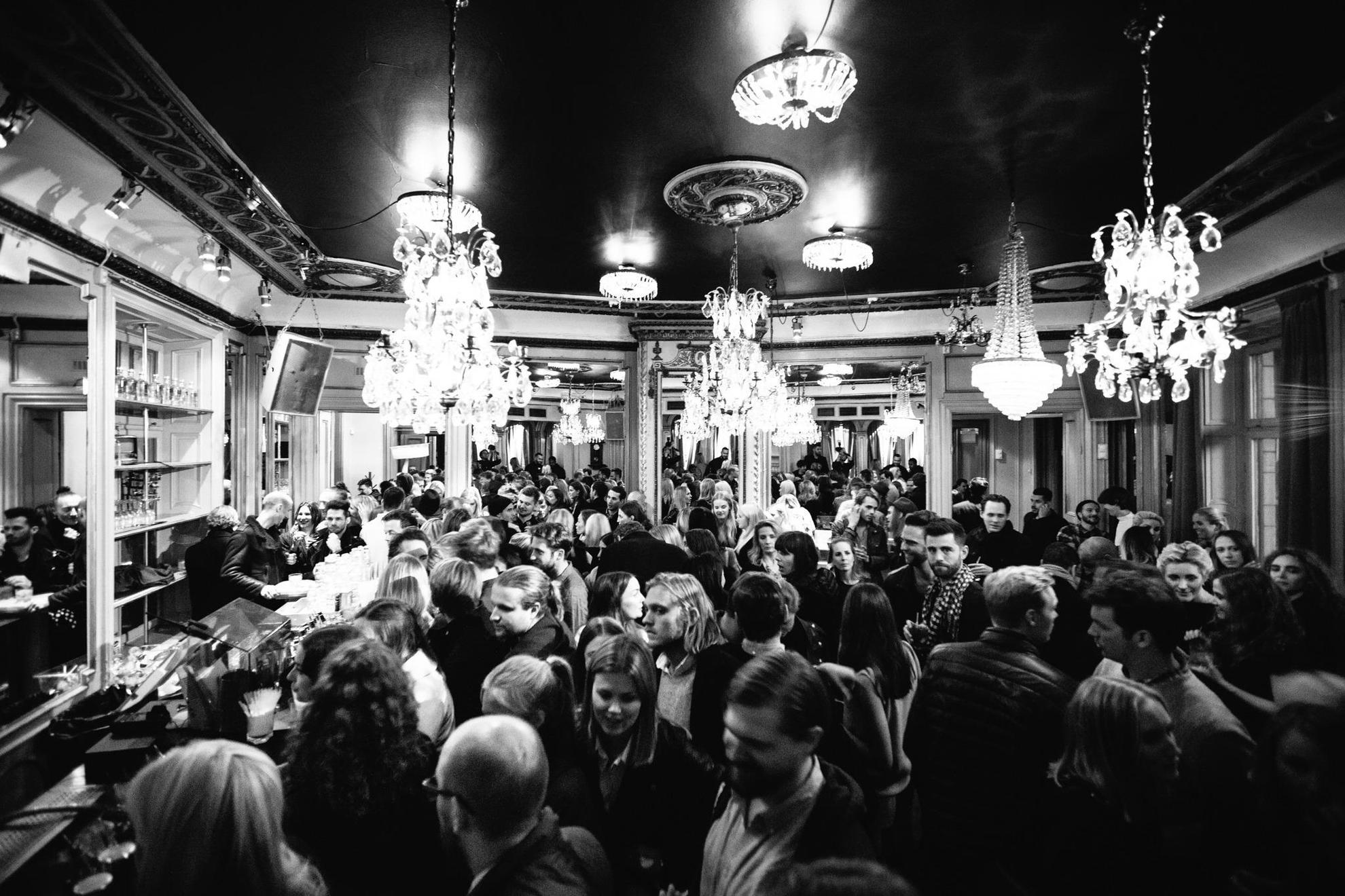 Ein Schwarz-Weiß-Bild von einer Menschenmenge in der Spy Bar in Stockholm. Kronleuchter hängen von der Decke.