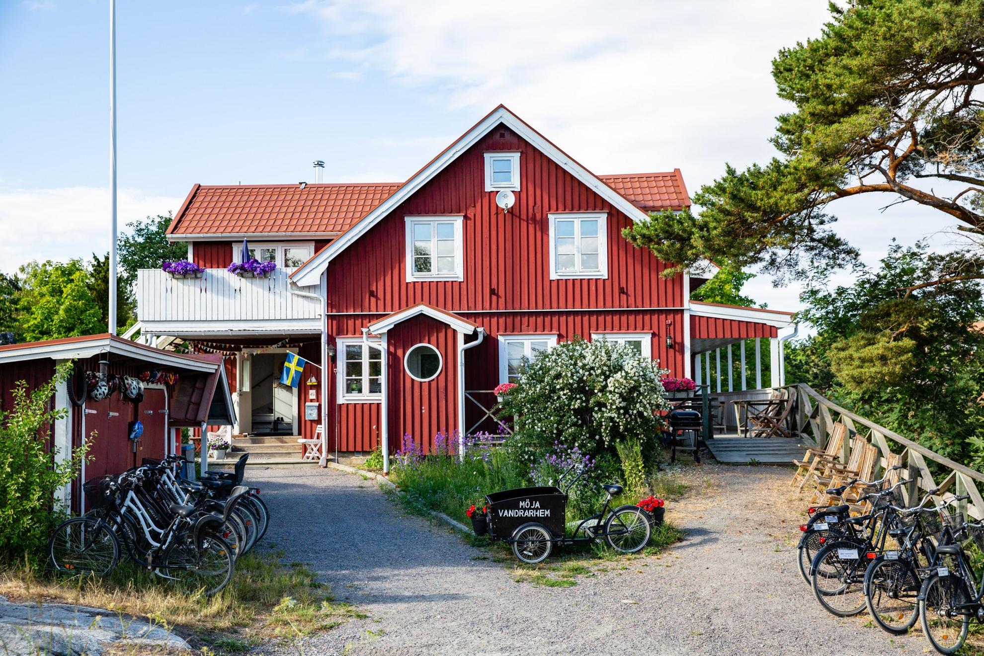 Ein rotes Holzhaus mit weißen Zierleisten im Sommer. Vor dem Haus stehen mehrere Fahrräder. Auf einem Fahrrad steht "Möja Vandrarhem".