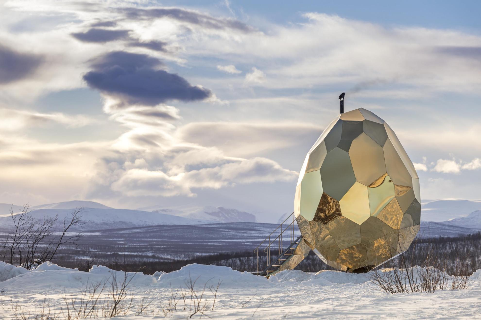 Eine holzbeheizte Sauna in Form eines Eies mit reflektierenden Laken, eingebettet in die arktische Winterlandschaft von Kiruna, die von Bergen und Schnee geprägt ist.