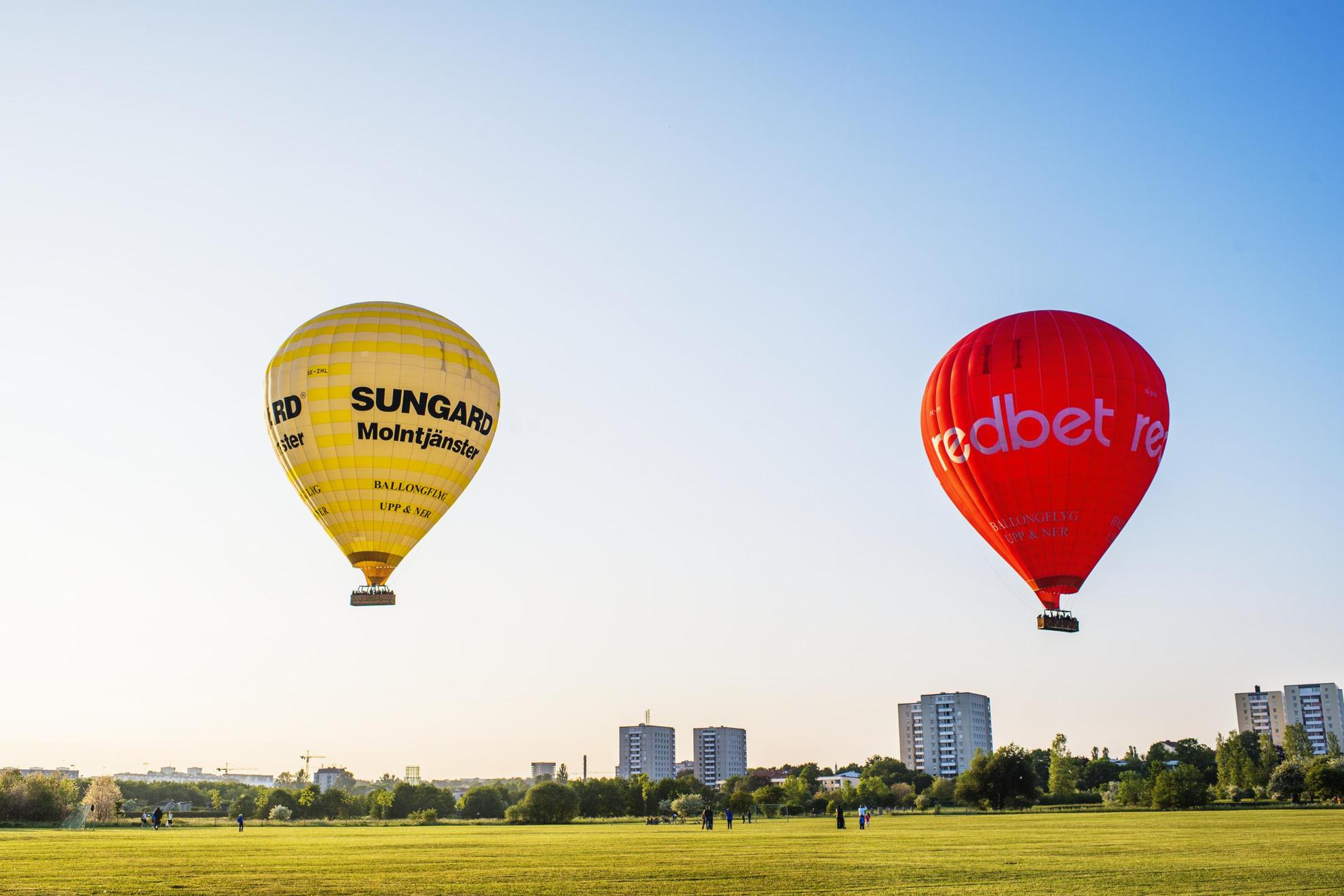 Hot air balloons gliding across the Stockholm skyline, over a park, high-rises in the background.