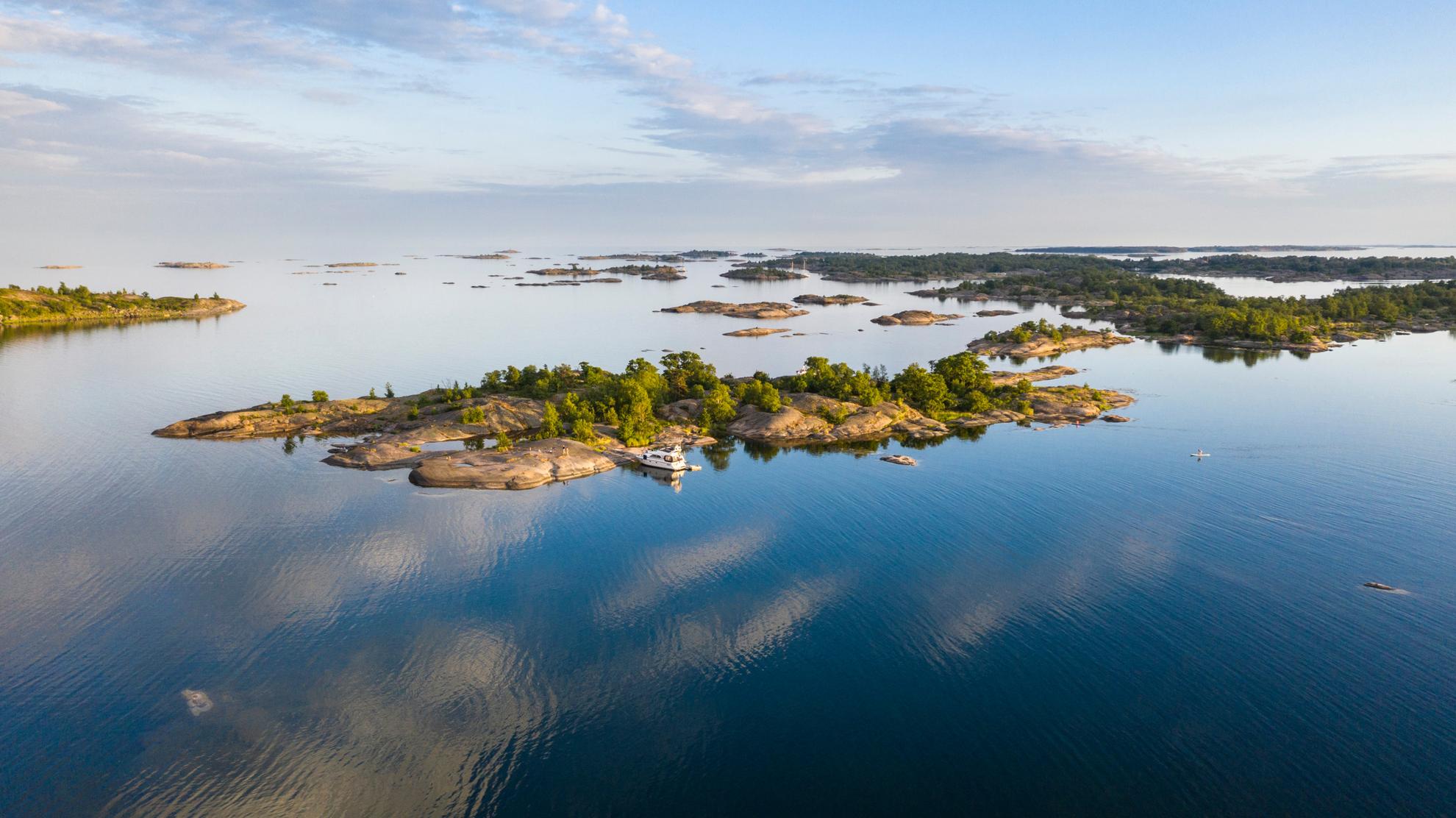 Luftaufnahme eines Bootes neben einer Insel im Stockholmer Schärengarten an einem Sommertag.