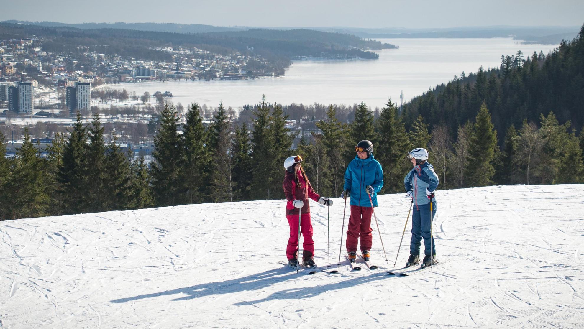 Drei Personen, die sich unterhalten, stehen auf einer Skipiste. Die Stadt Ulricehamn liegt im Hintergrund.