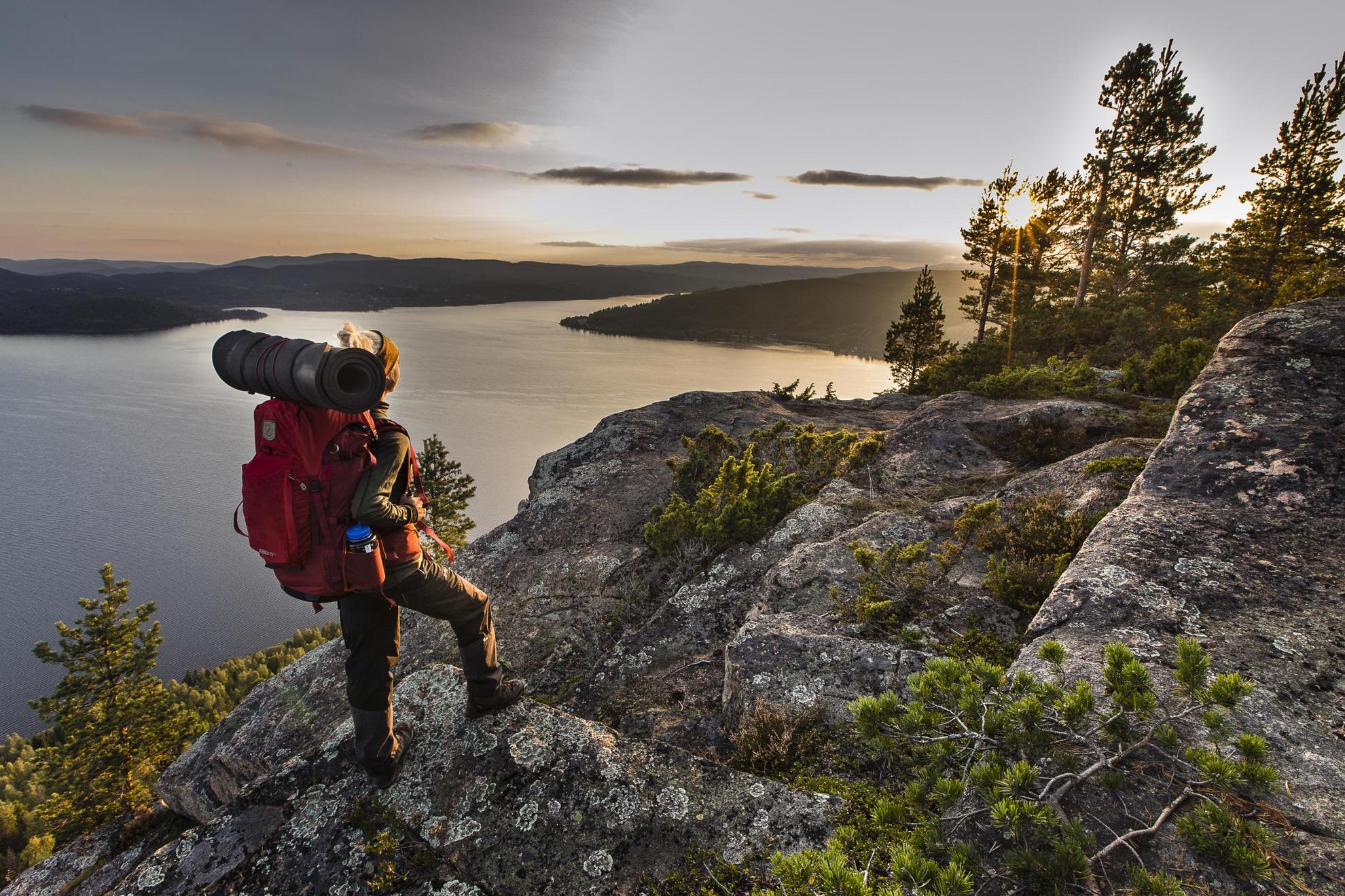 Eine Frau mit Rucksack steht auf einem Berg mit Blick auf die Küste, während die Sonne untergeht.