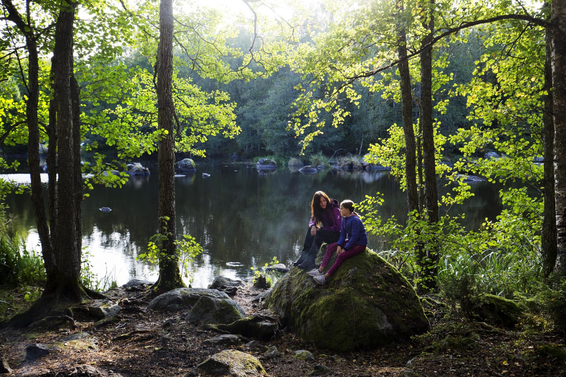 Zwei Mädchen sitzen auf einem Felsen neben einem See in der Natur.