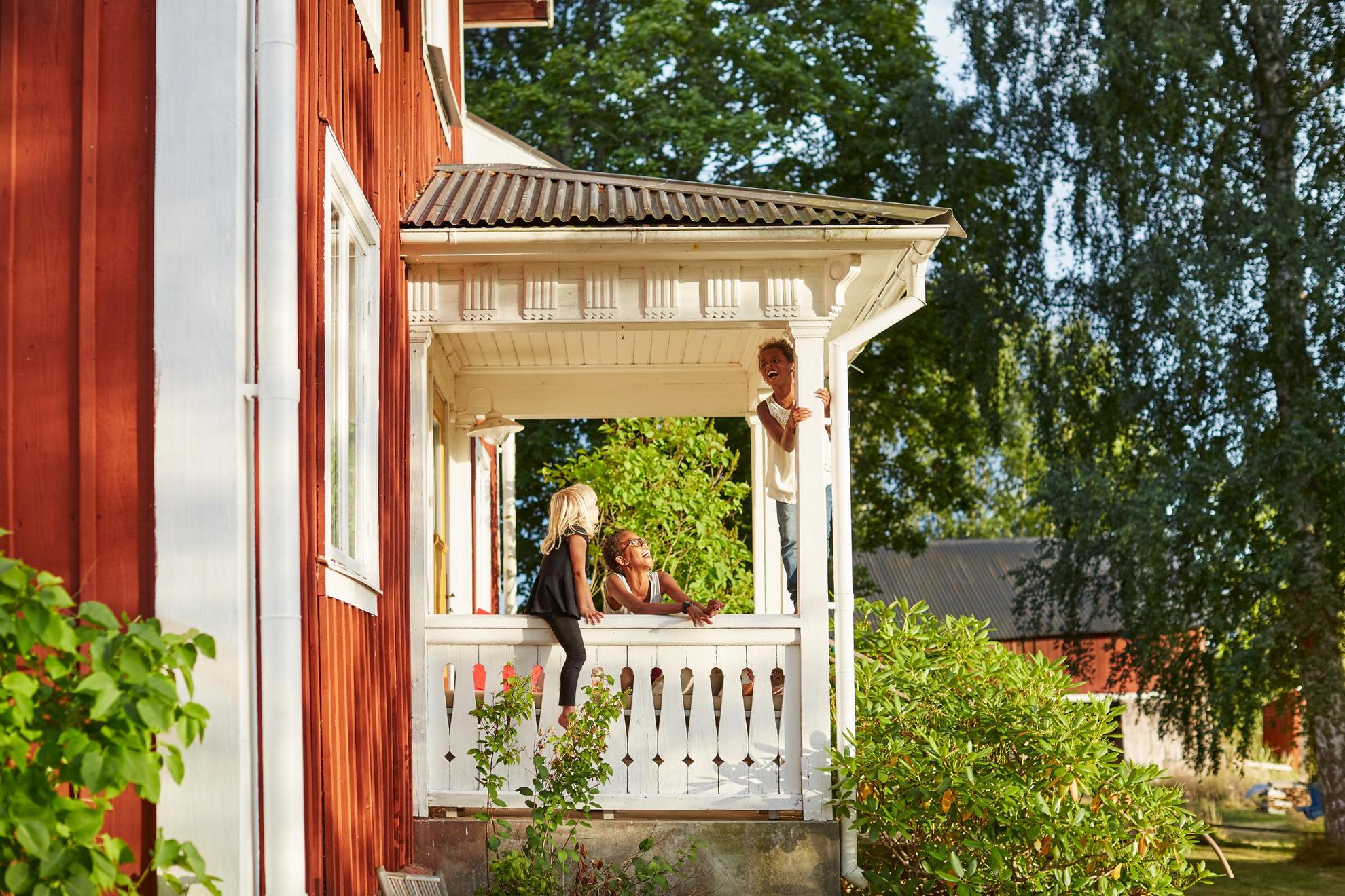 Kinder toben auf der Terrasse eines roten schwedischen Holzhauses.