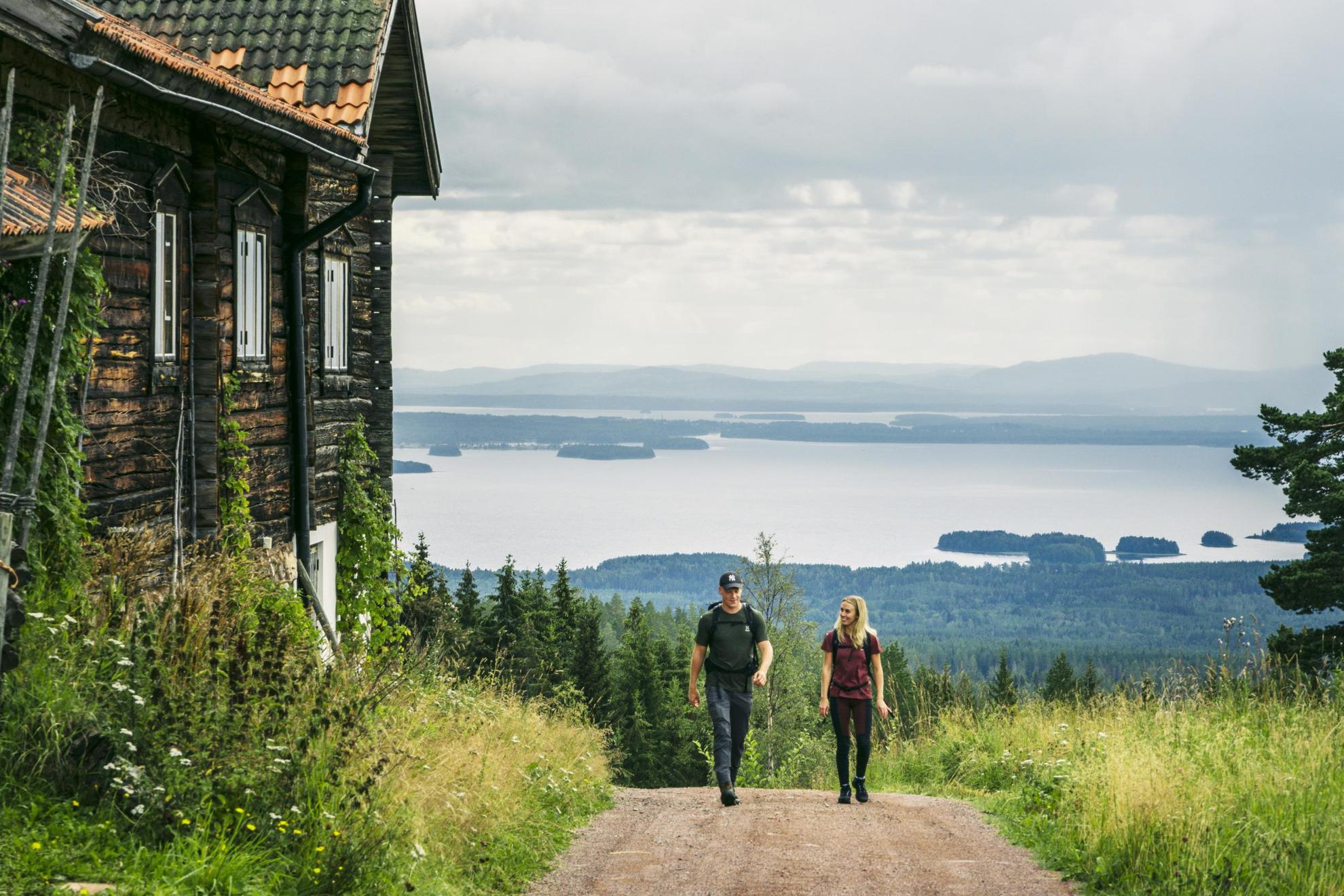 Zwei Menschen Wandern entlang einer Holzhütte in der Natur Dalarnas.